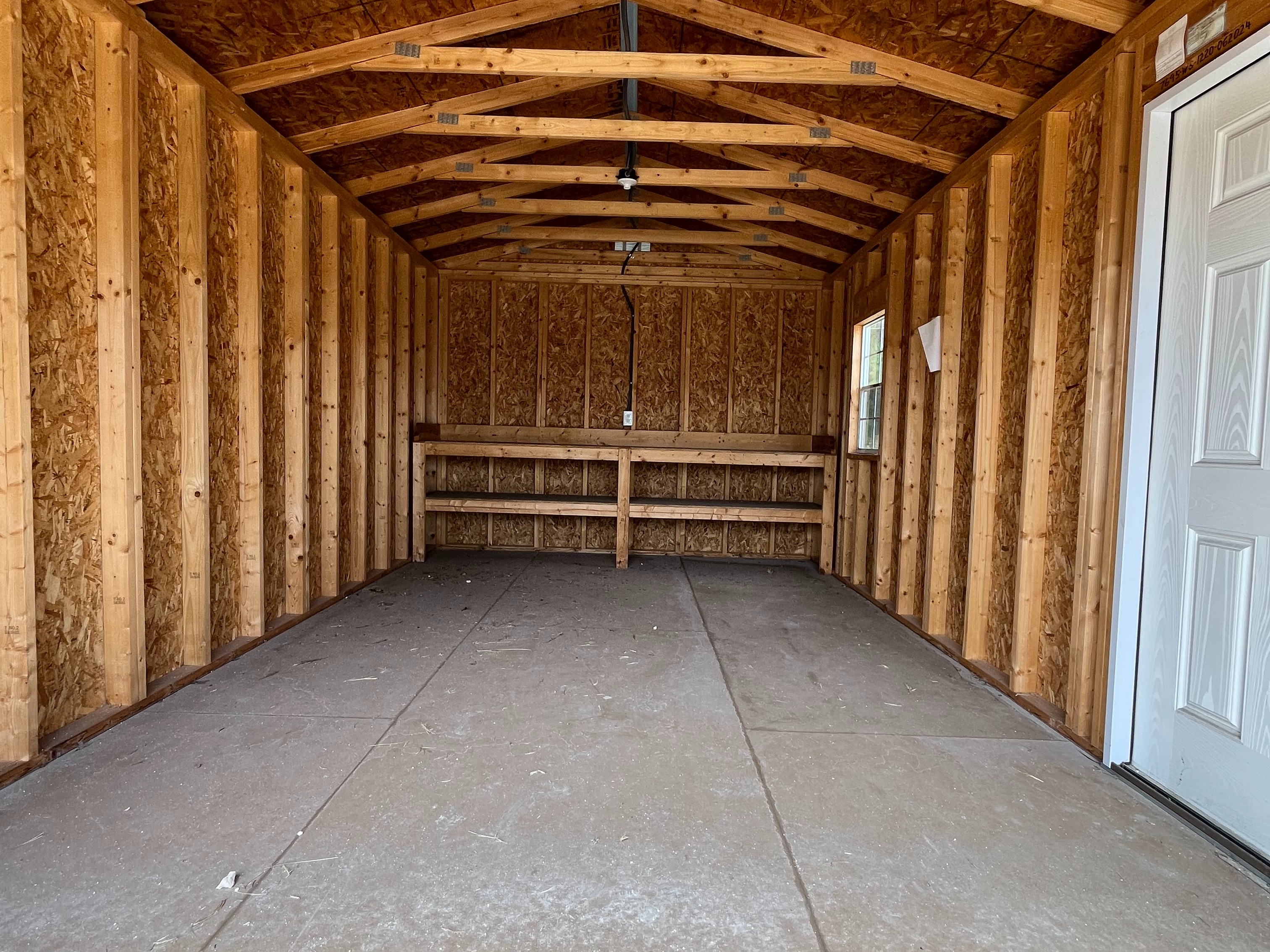 interior view of a workshop shed through the garage door showing a walk-in door, window, and workbench in the back