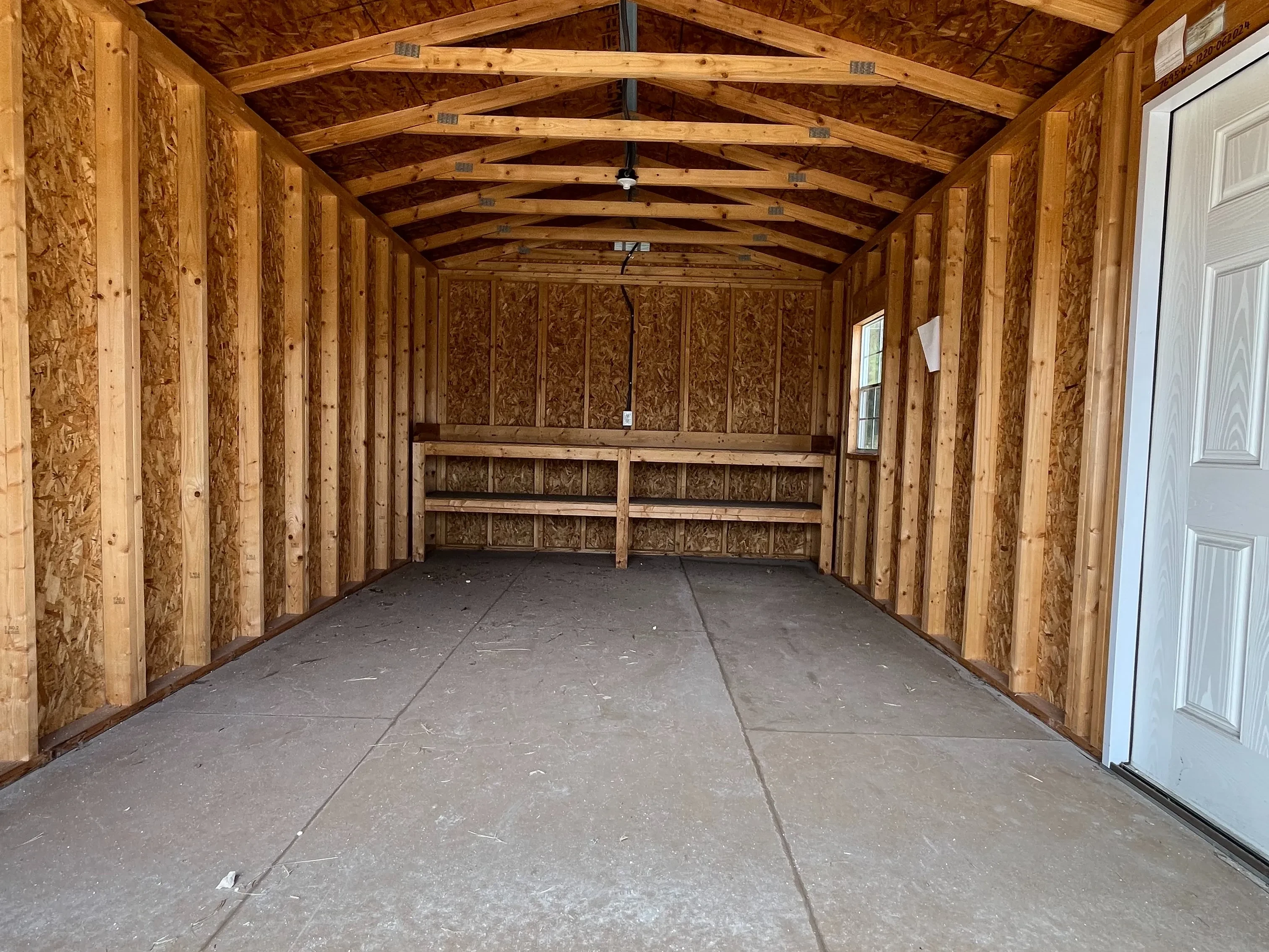 Interior view of a workshop shed through the garage door showing a walk-in door, window, and workbench in the back