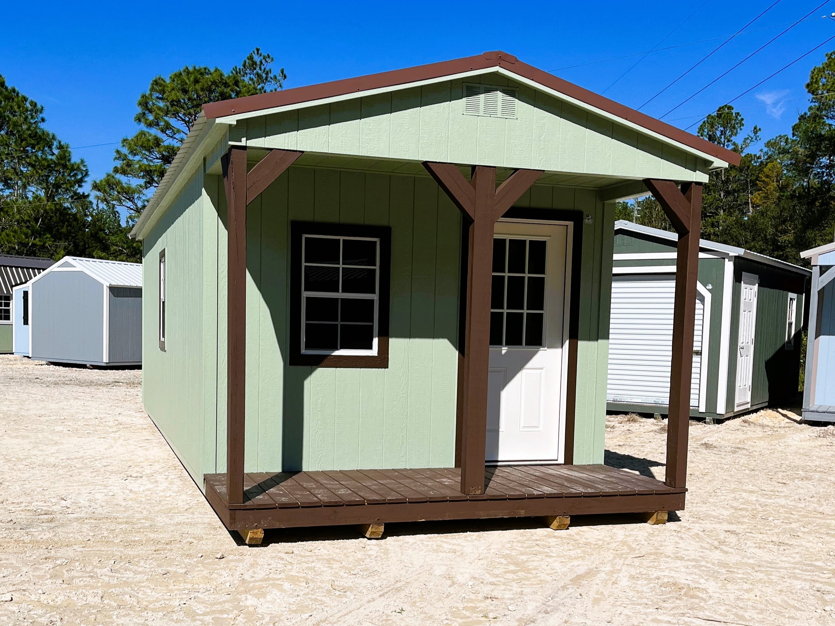 Outside of a sage green 12x28 cabin, has a porch with a walk-in door and window 