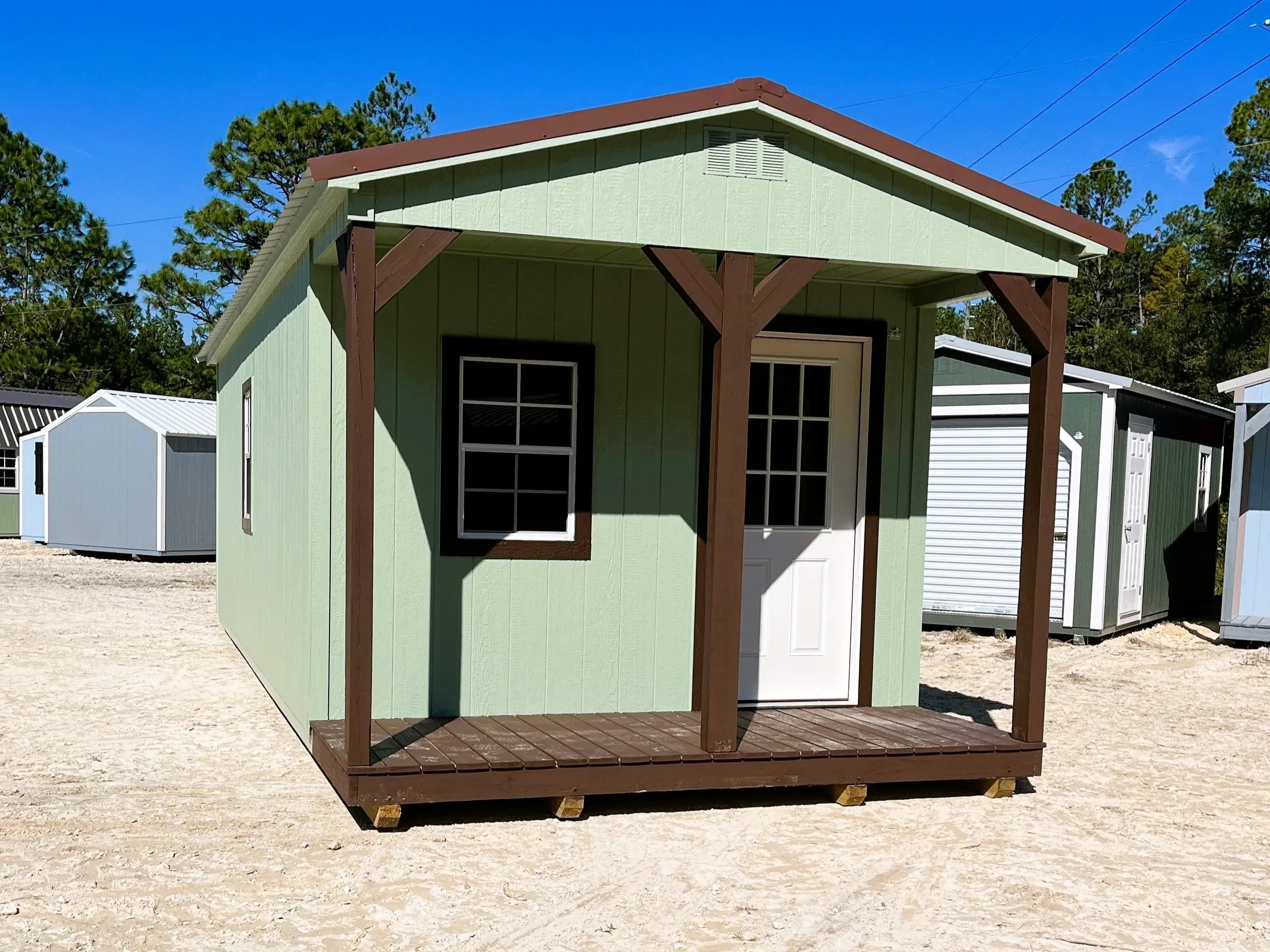 Outside of a sage green 12x28 cabin, has a porch with a walk-in door and window