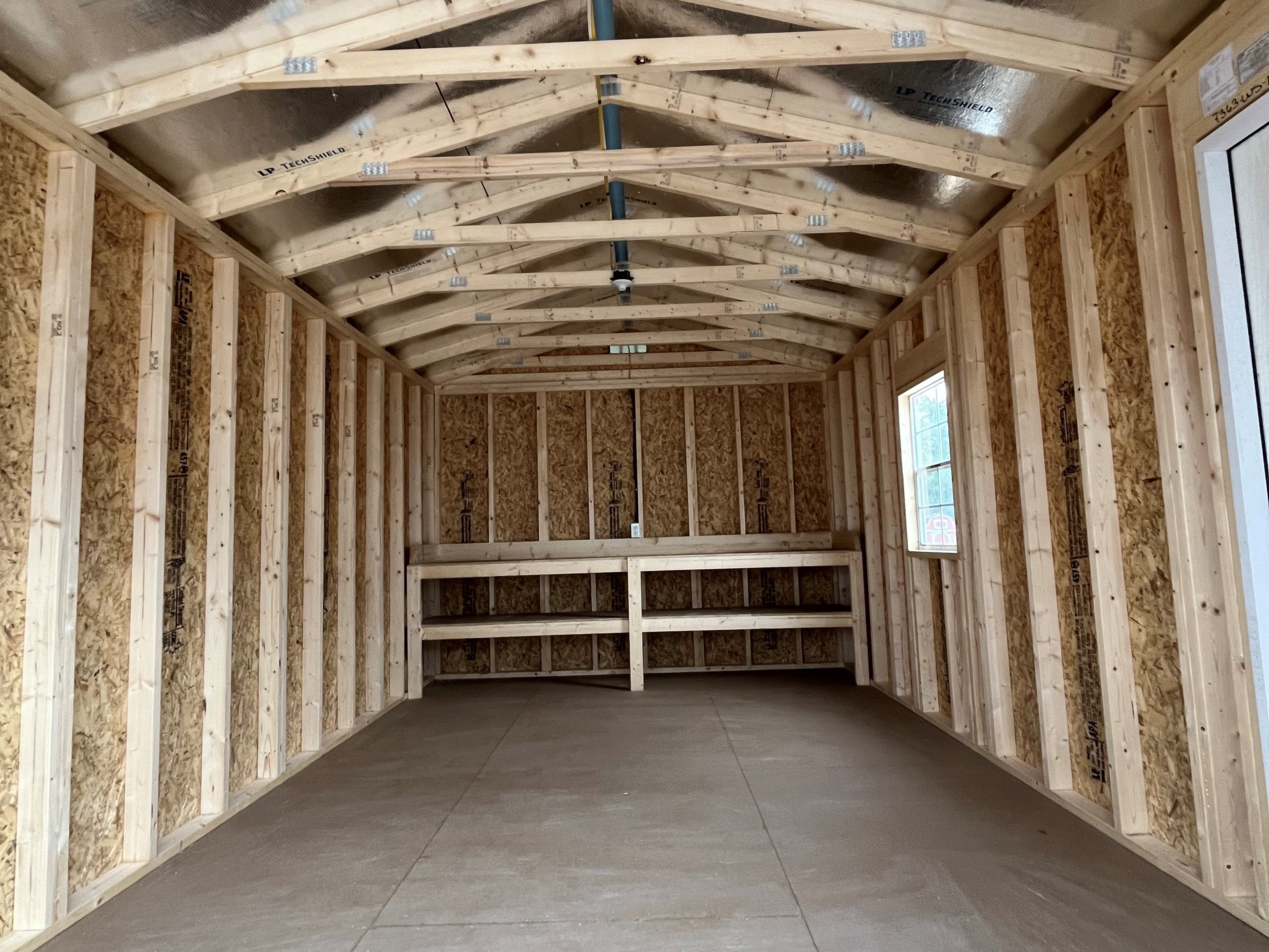 Interior view of the workshop shed through the garage door showing a walk-in door, window, and workbench in the back