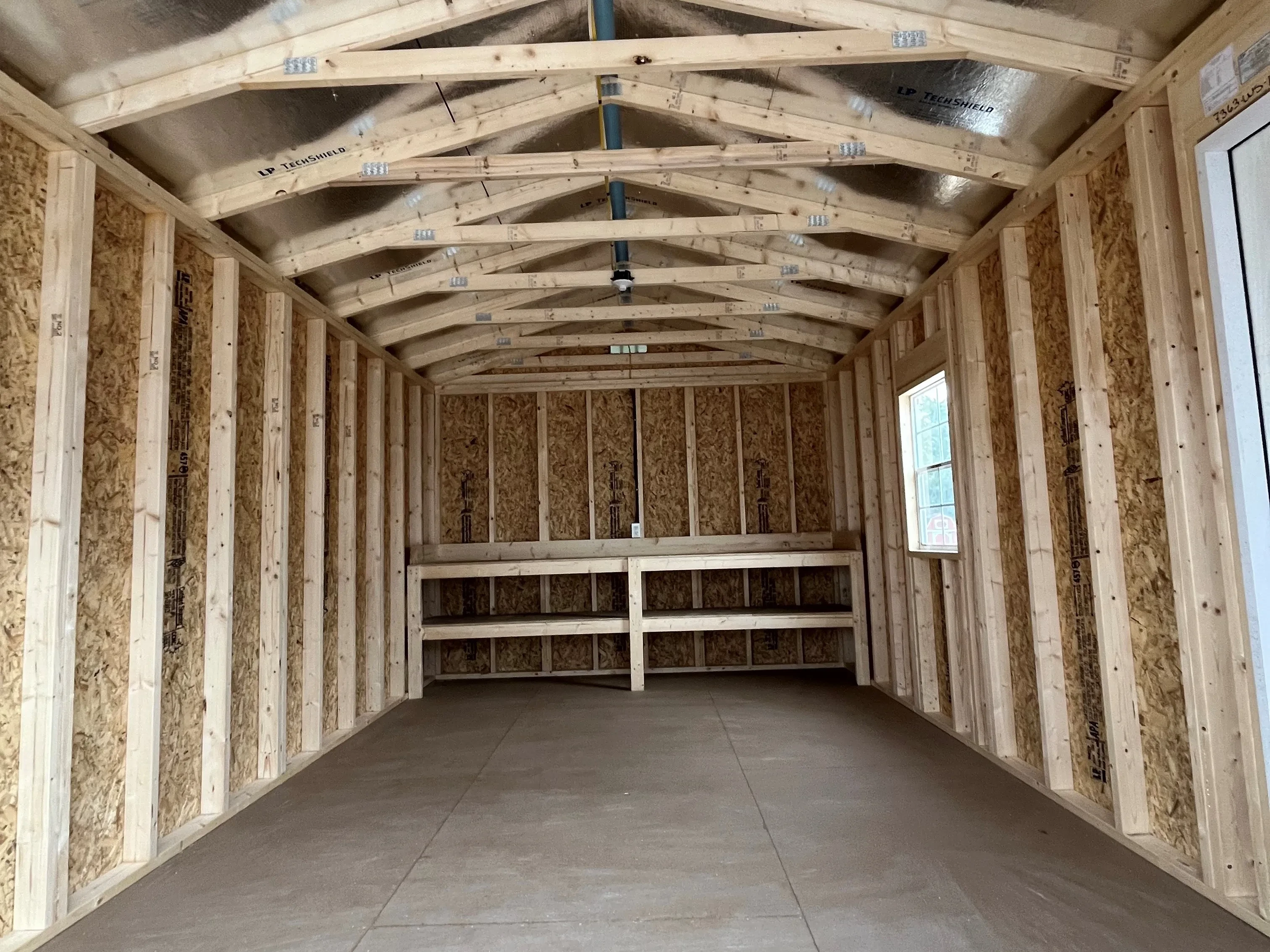 Interior view of the workshop shed through the garage door showing a walk-in door, window, and workbench in the back