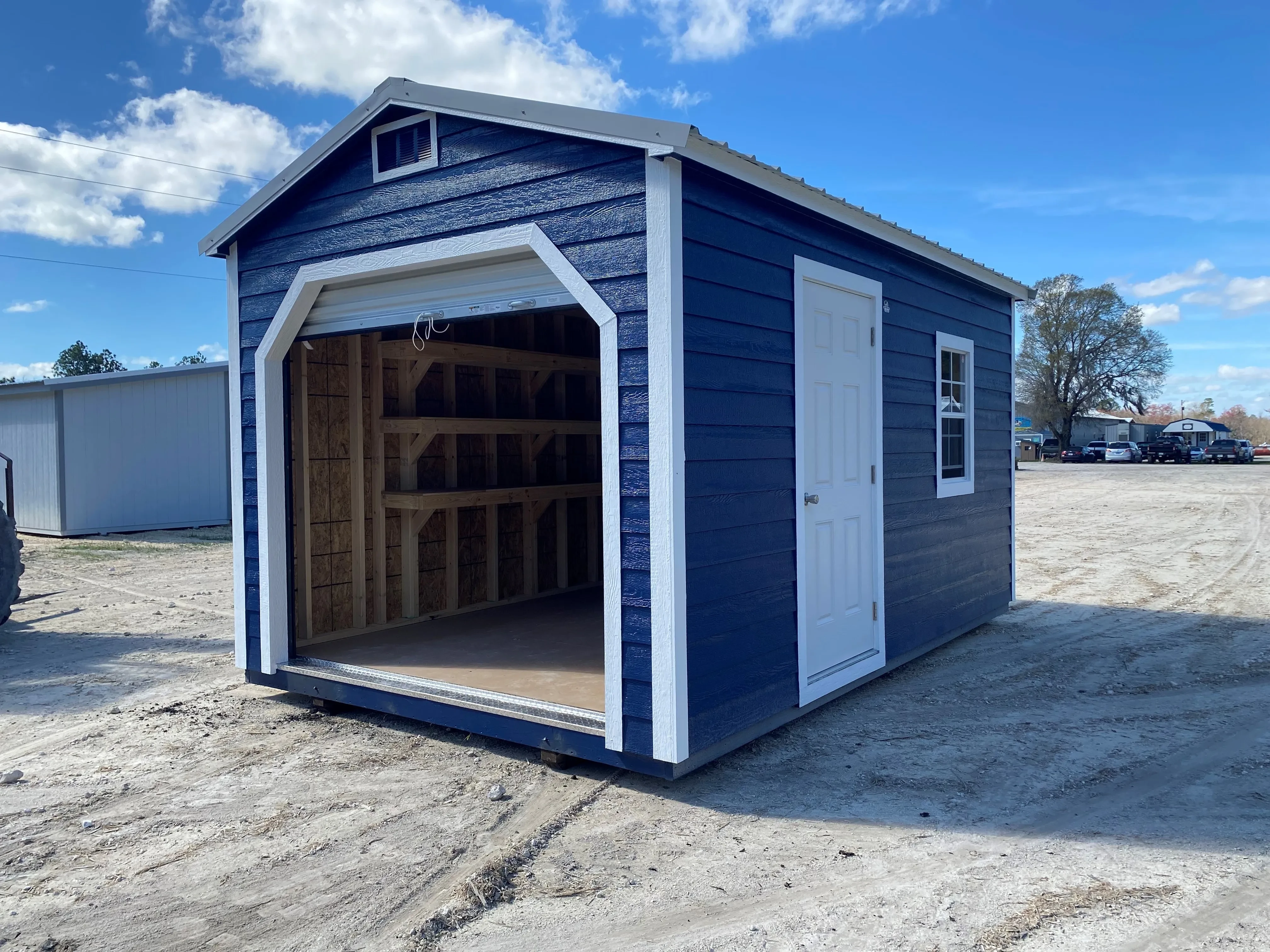 Exterior of a dark blue 10x16 workshop shed showing a garage door, walk-in door and window