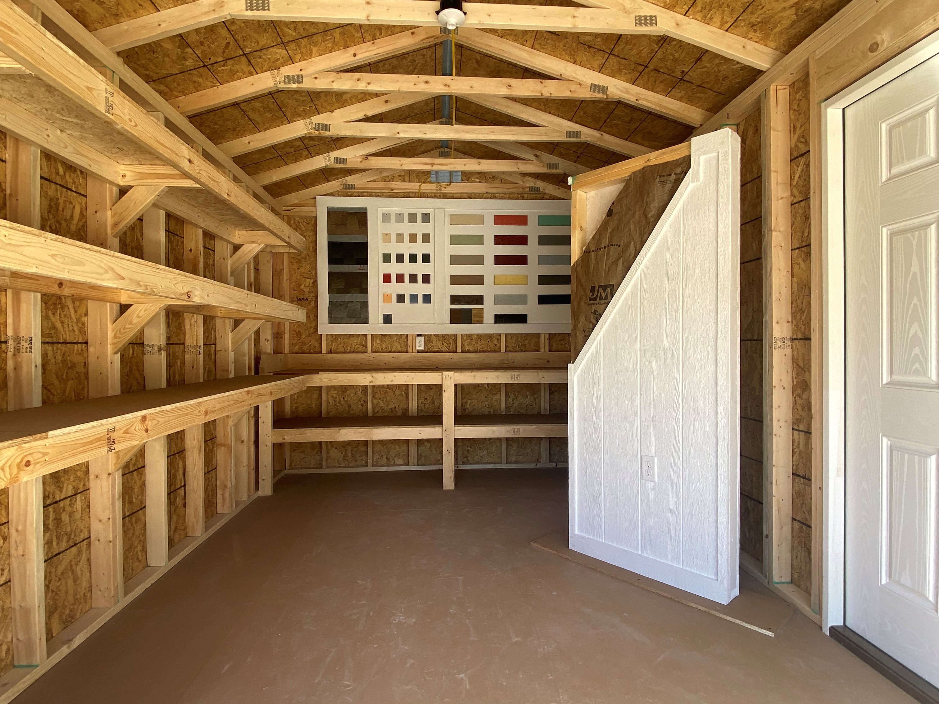 Interior of a 10x16 workshop shed showing through the garage door, has shelving on the left and workbench on the back wall