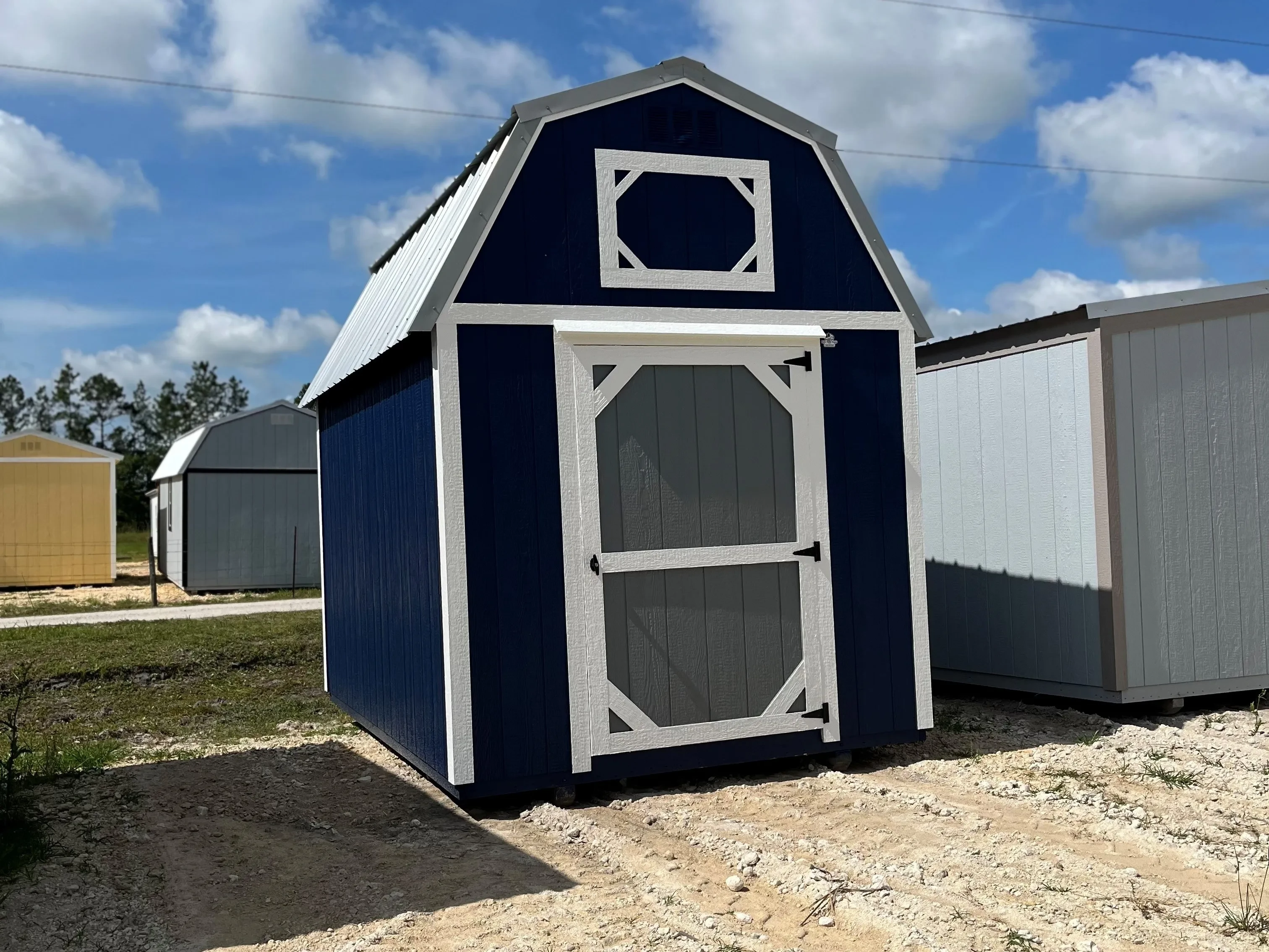 Exterior of a dark blue 8x12 lofted barn with a single wood door painted grey
