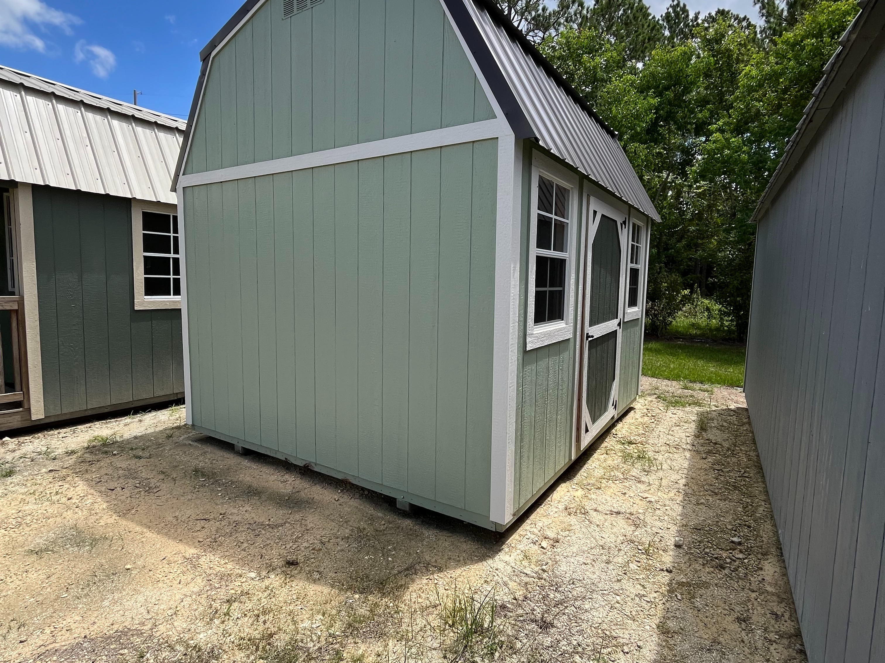 Exterior side view of sage green a 10x12 side lofted barn with a single wood door and windows