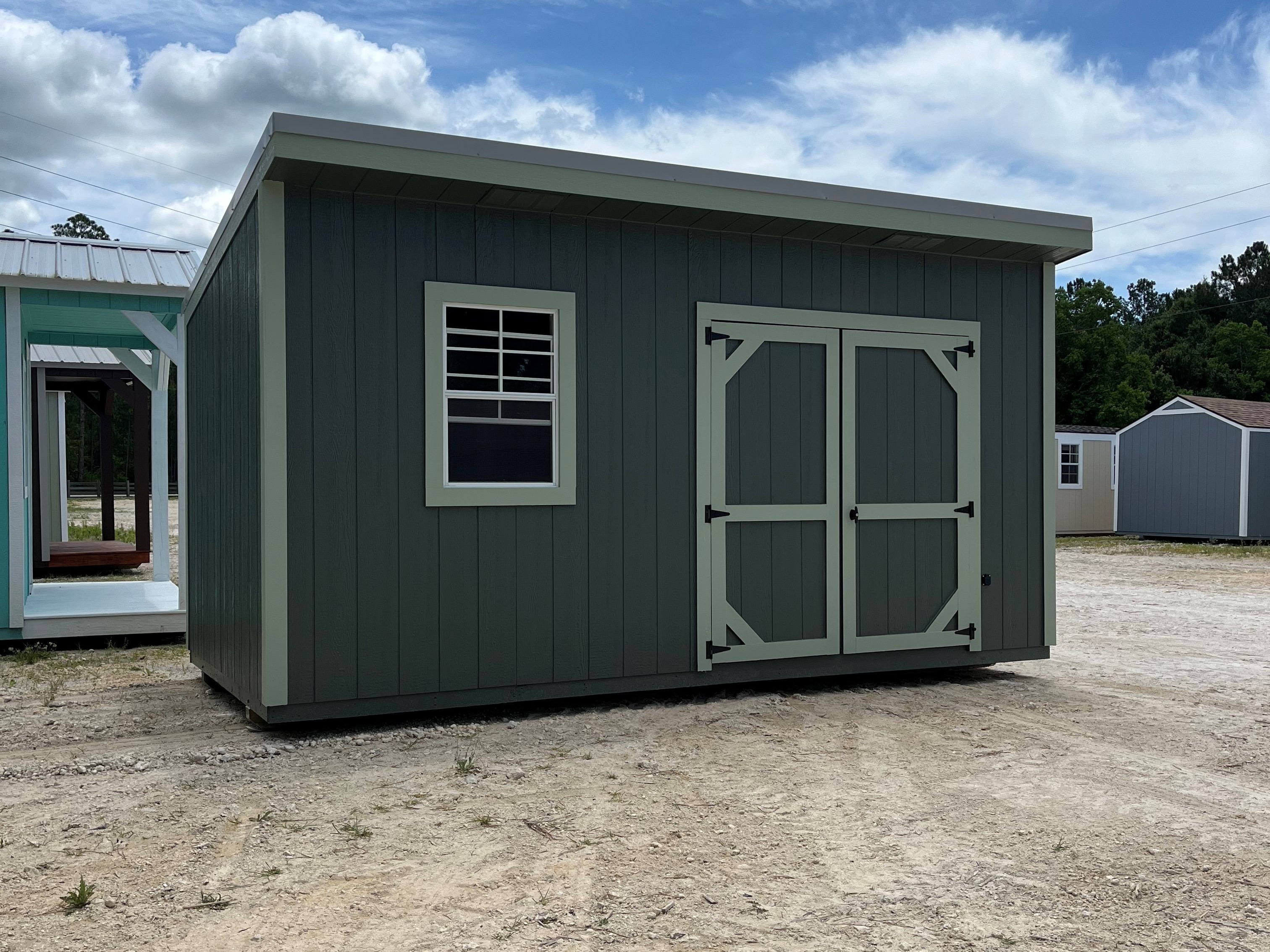 Outside of a green 8x16 urban shed with double wood doors and a window
