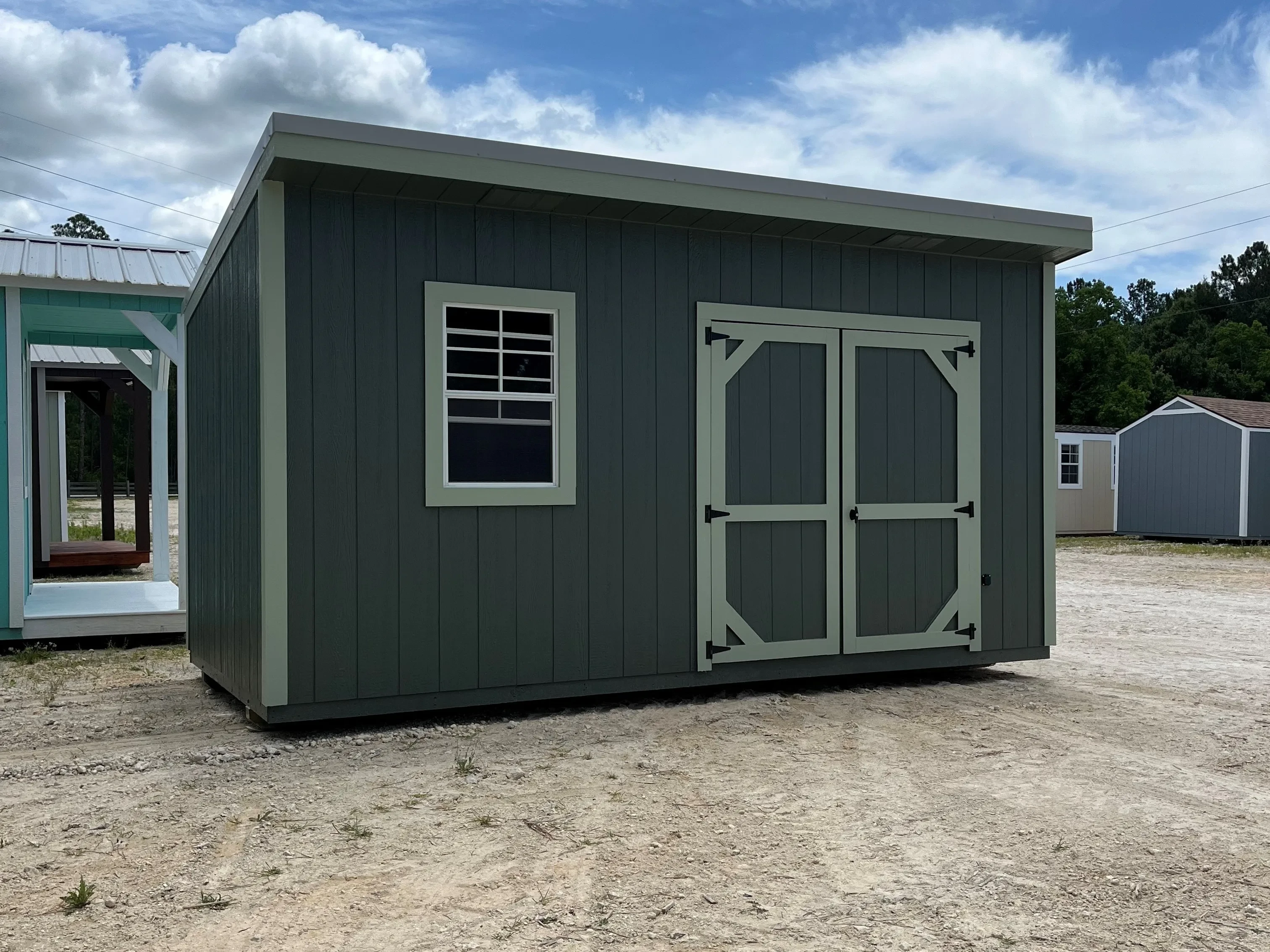Outside of a green 8x16 urban shed with double wood doors and a window