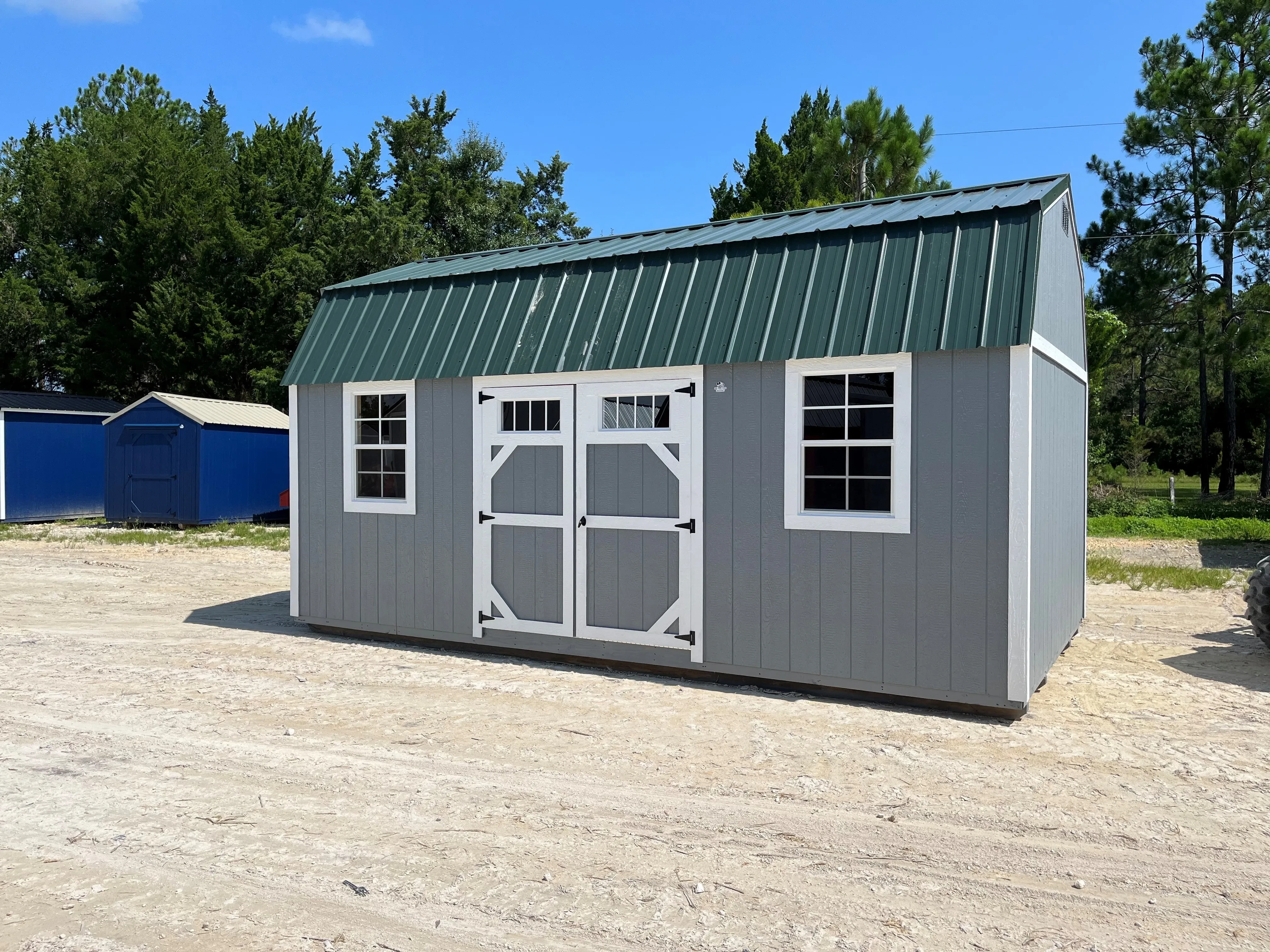 Outside of a grey 12x20 side lofted barn with double wood doors with transom in door, two windows, and a metal roof