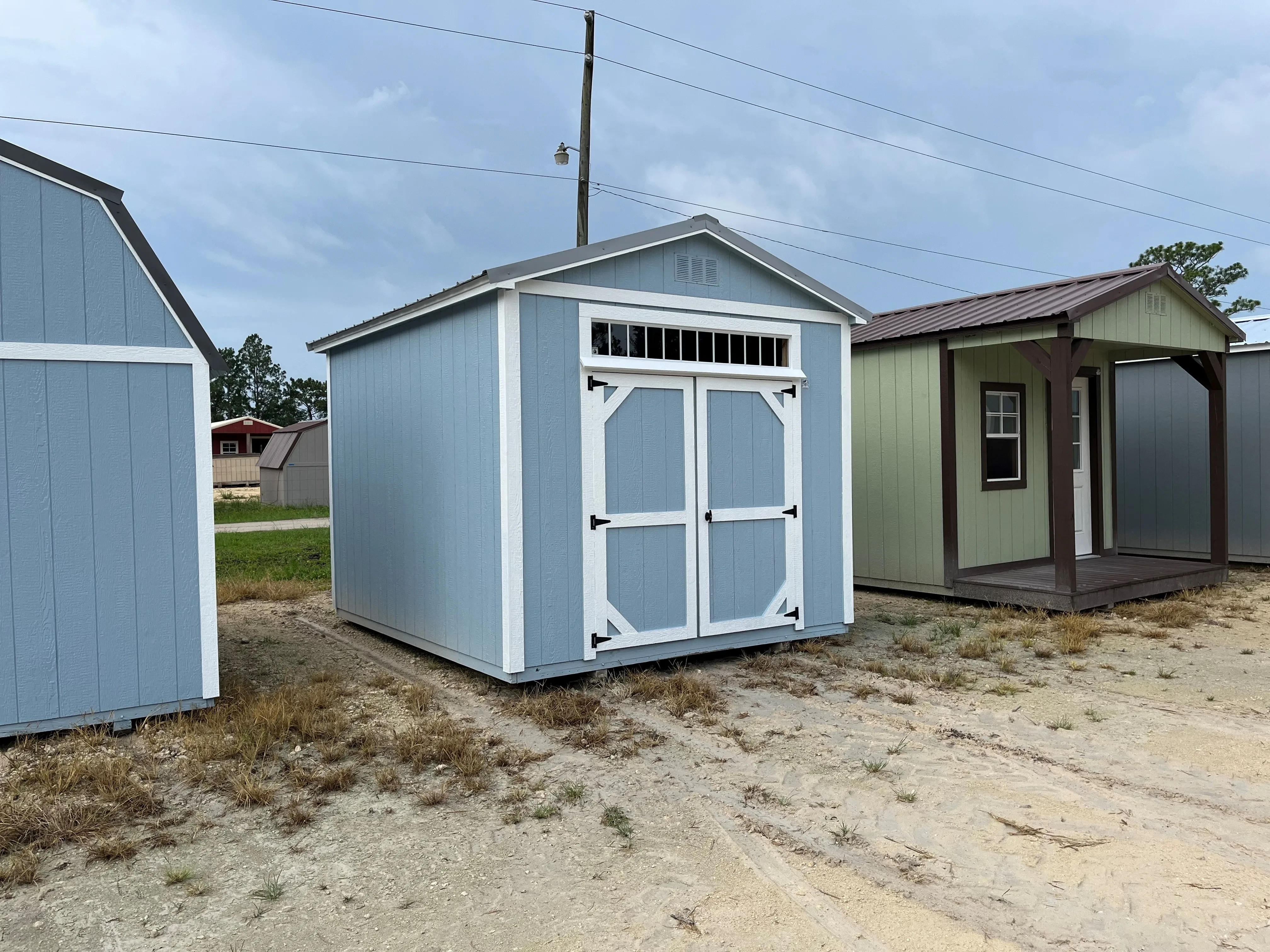 Outside of a blue 10x12 garden shed with double wood doors and a large transom window