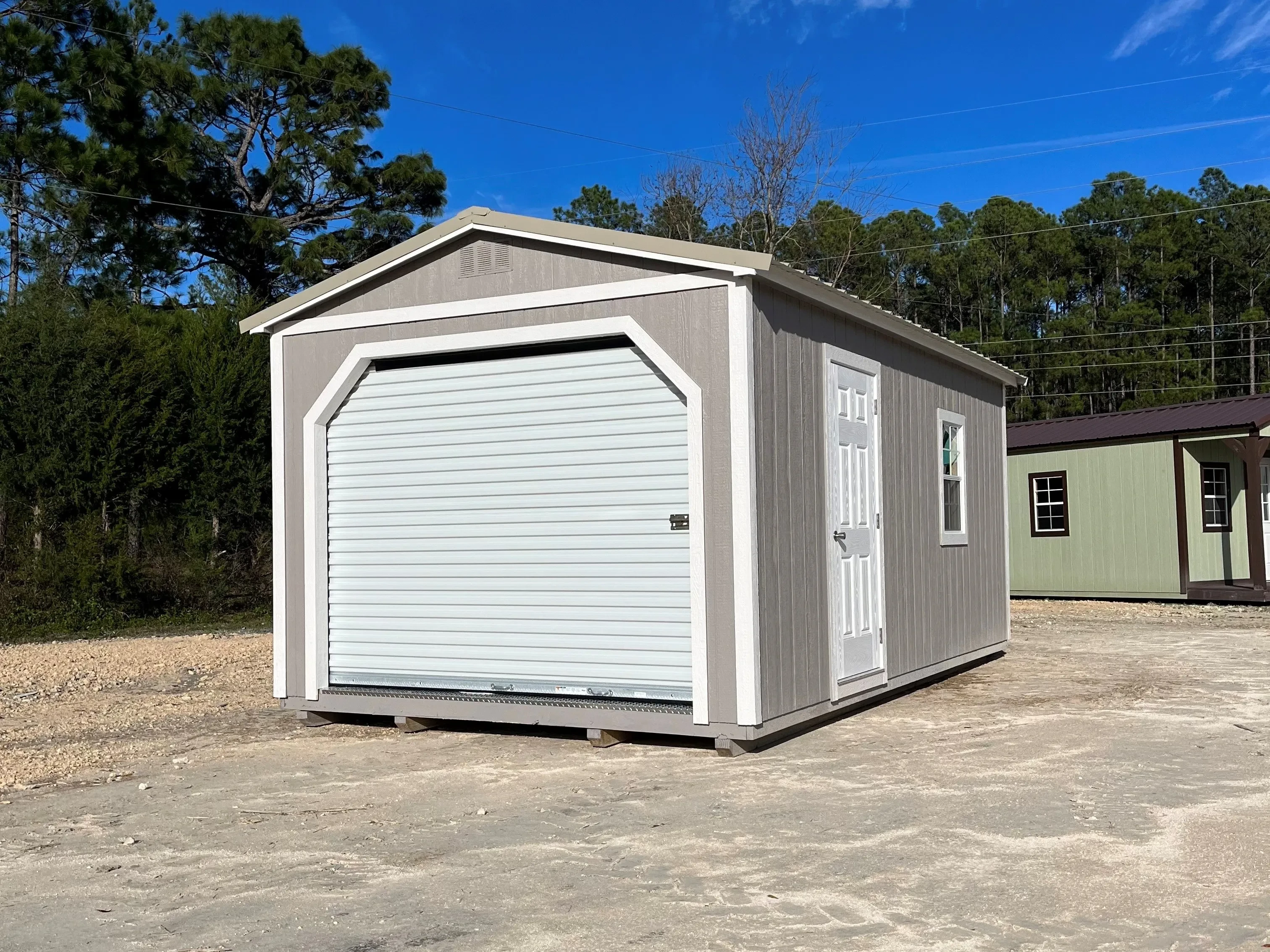 Outside view of a 12x20 taupe painted workshop showing rollup door on the front and an entry door and window on the side