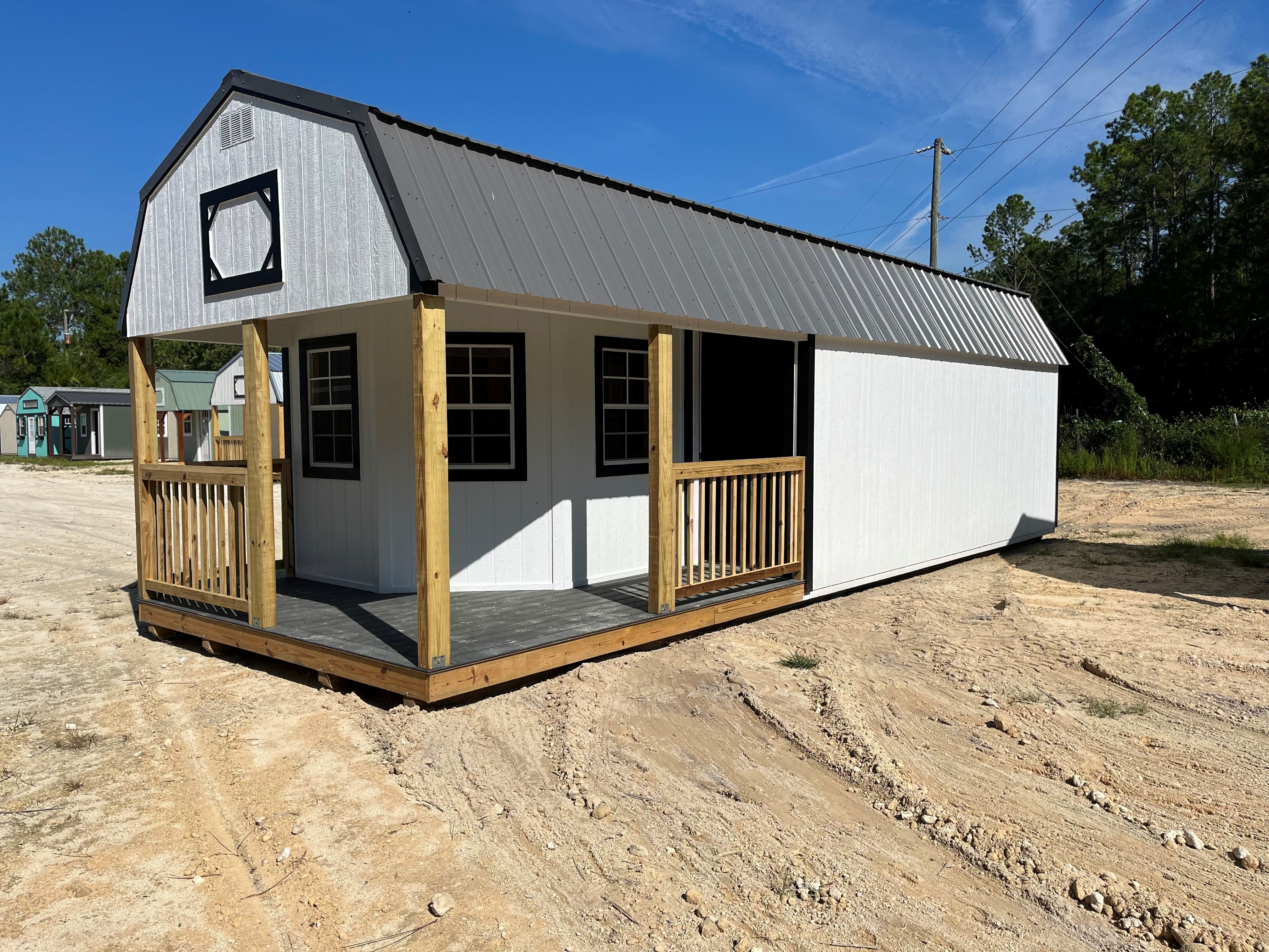 Outside of a white 12x32 deluxe lofted barn cabin showing a wrap around porch with rails, three windows, and a metal roof