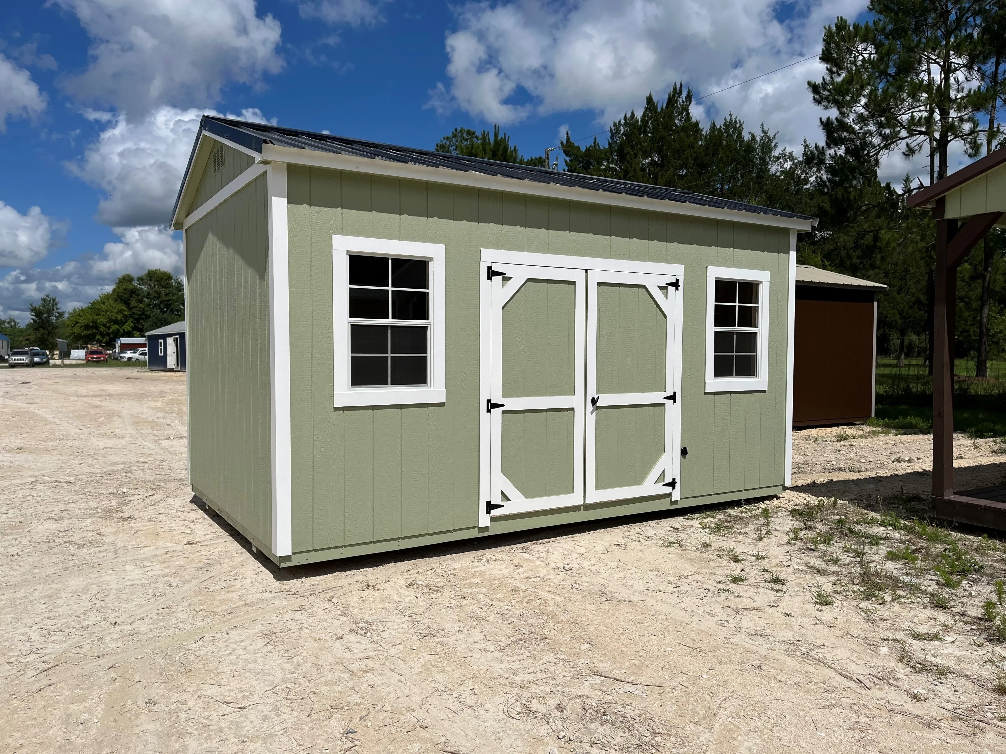 Exterior of a green 10x16 side garden shed with double wood doors and windows