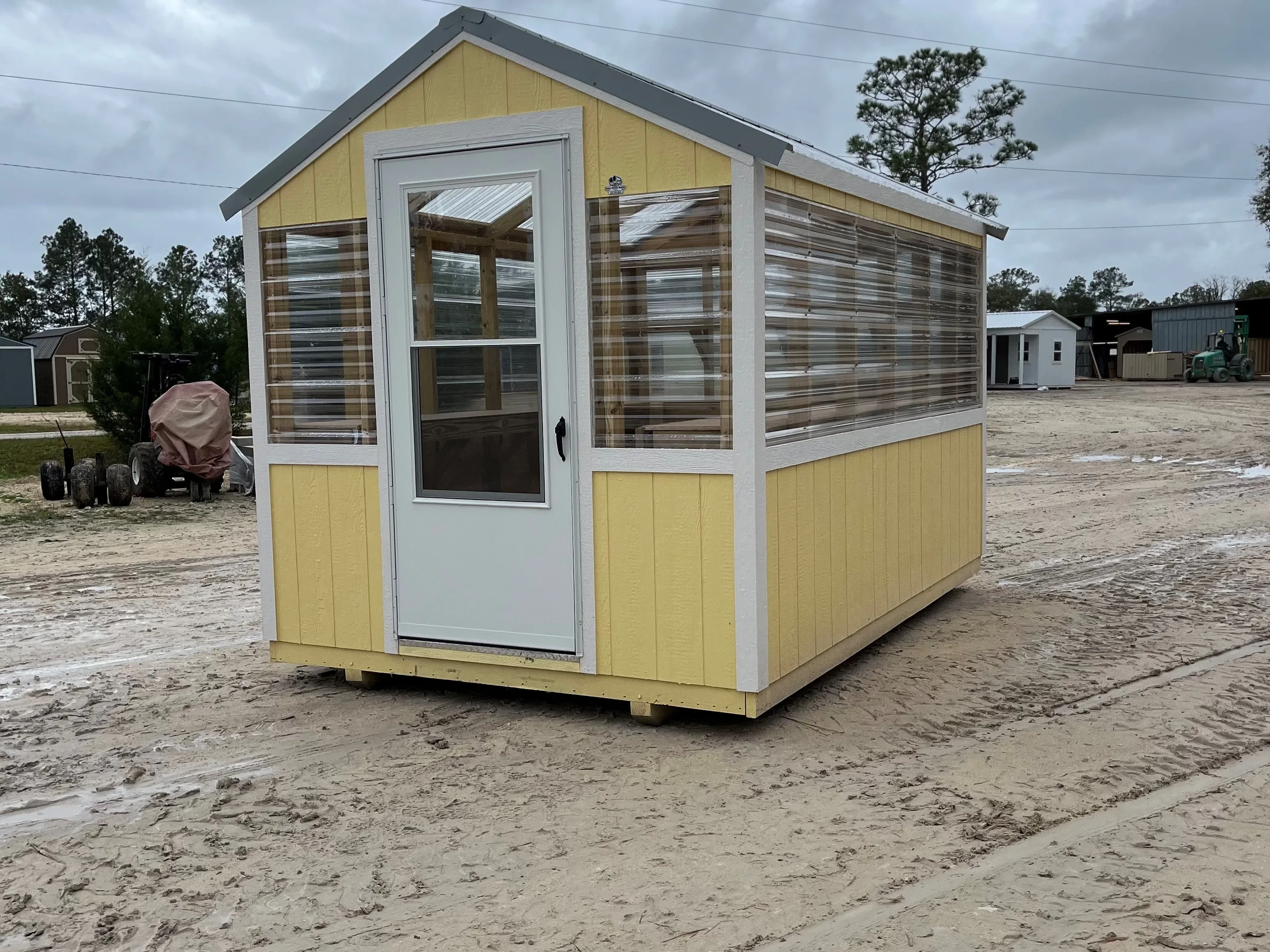 Outside of an 8x12 yellow and clear greenhouse with white trim and an entry door