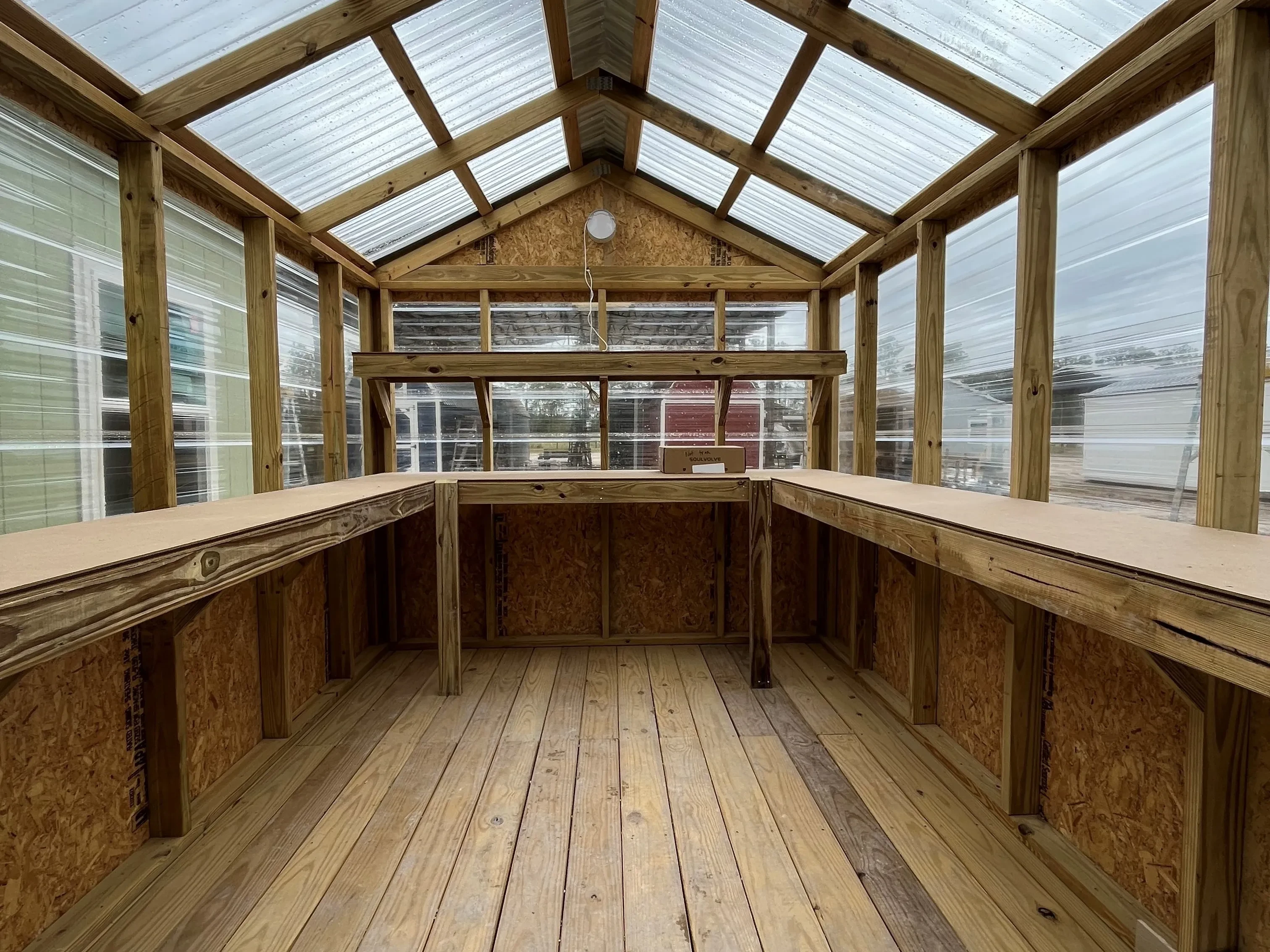 Interior of an 8x12 greenhouse with clear panels on top, wood panels on bottom, a workbench, and a solar exhaust fan