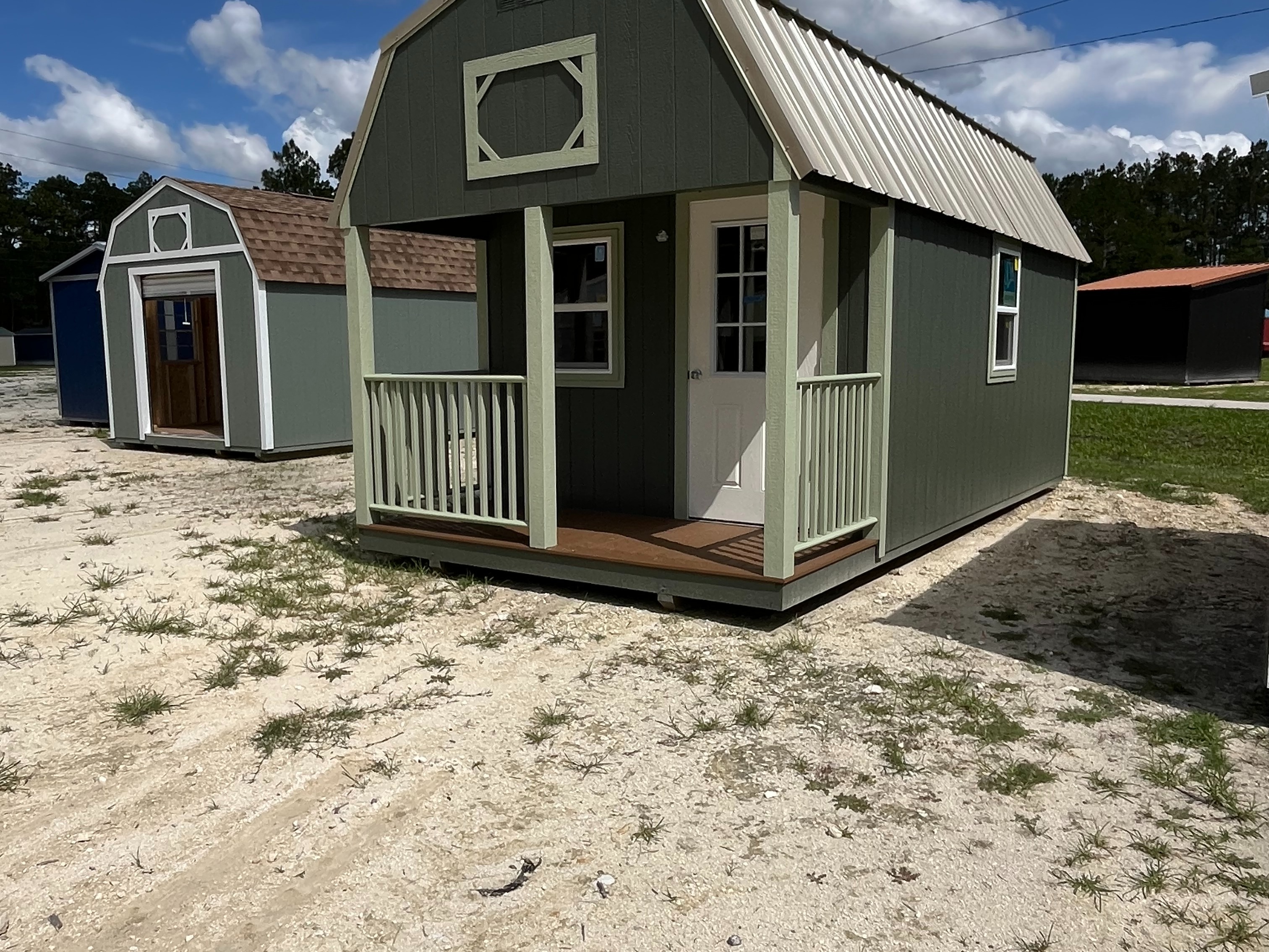 Outside of a dark green 10x20 lofted barn cabin showing an entry door,  windows, and front porch with light green railing