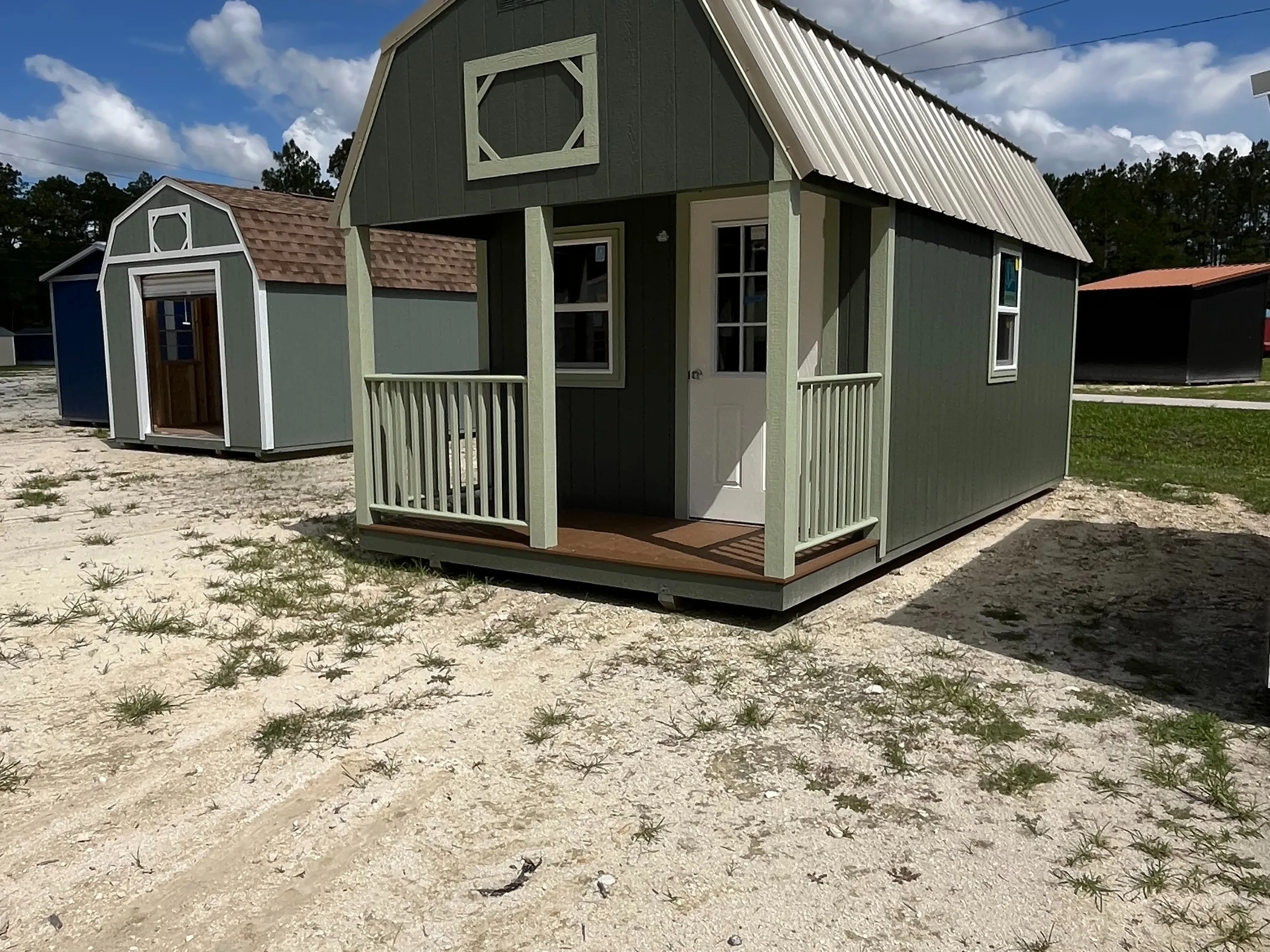Outside of a dark green 10x20 lofted barn cabin showing an entry door, windows, and front porch with light green railing