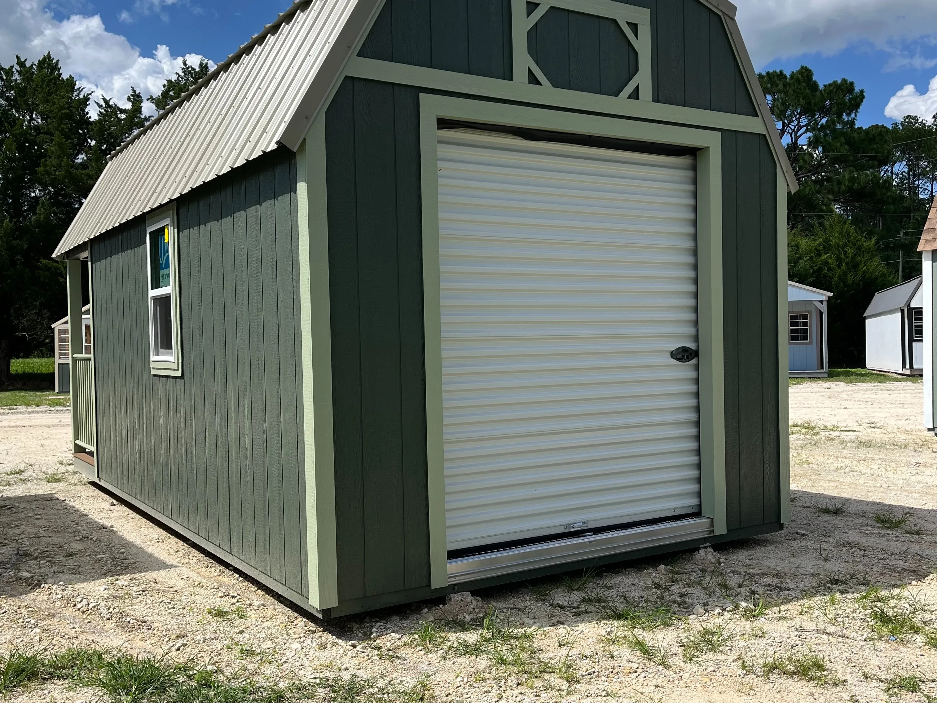 Outside of a dark green 10x20 lofted barn cabin showing a rollup door on the back of the cabin and a window on the side