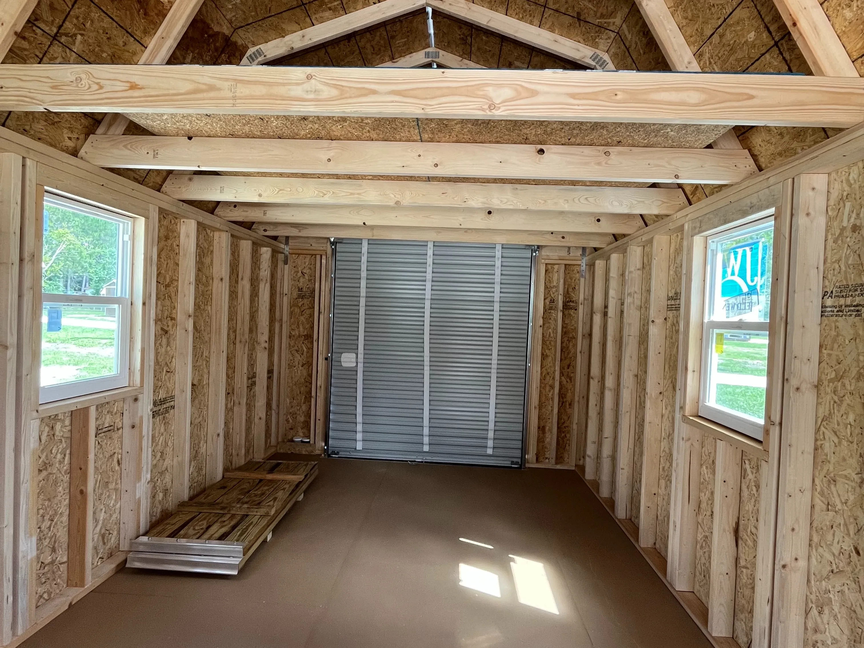Inside of a 10x20 lofted barn cabin showing a loft, inside of the roll up door, two windows, and ramps