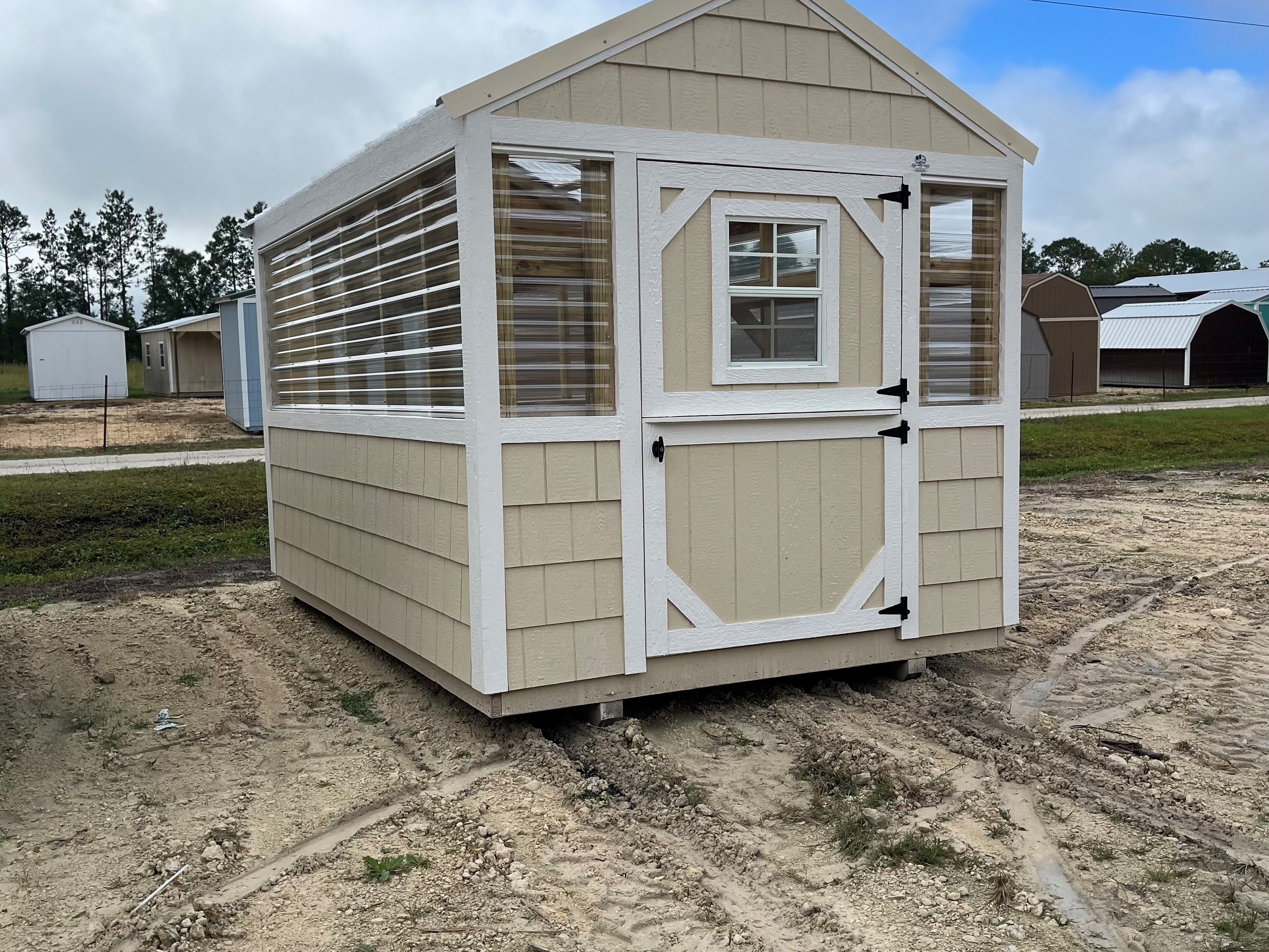 Outside of an almond painted 8x12 greenhouse, showing entry door, windows, and side of building