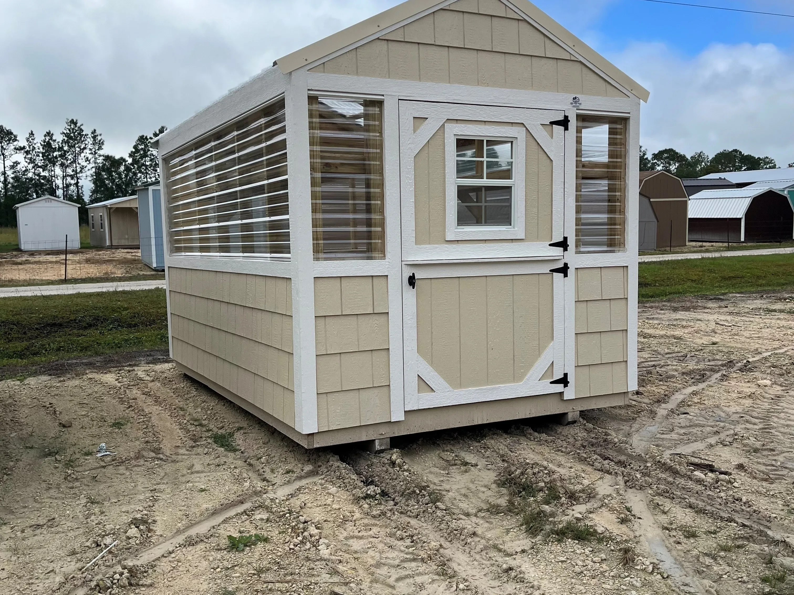 Outside of an almond painted 8x12 greenhouse, showing entry door, windows, and side of building