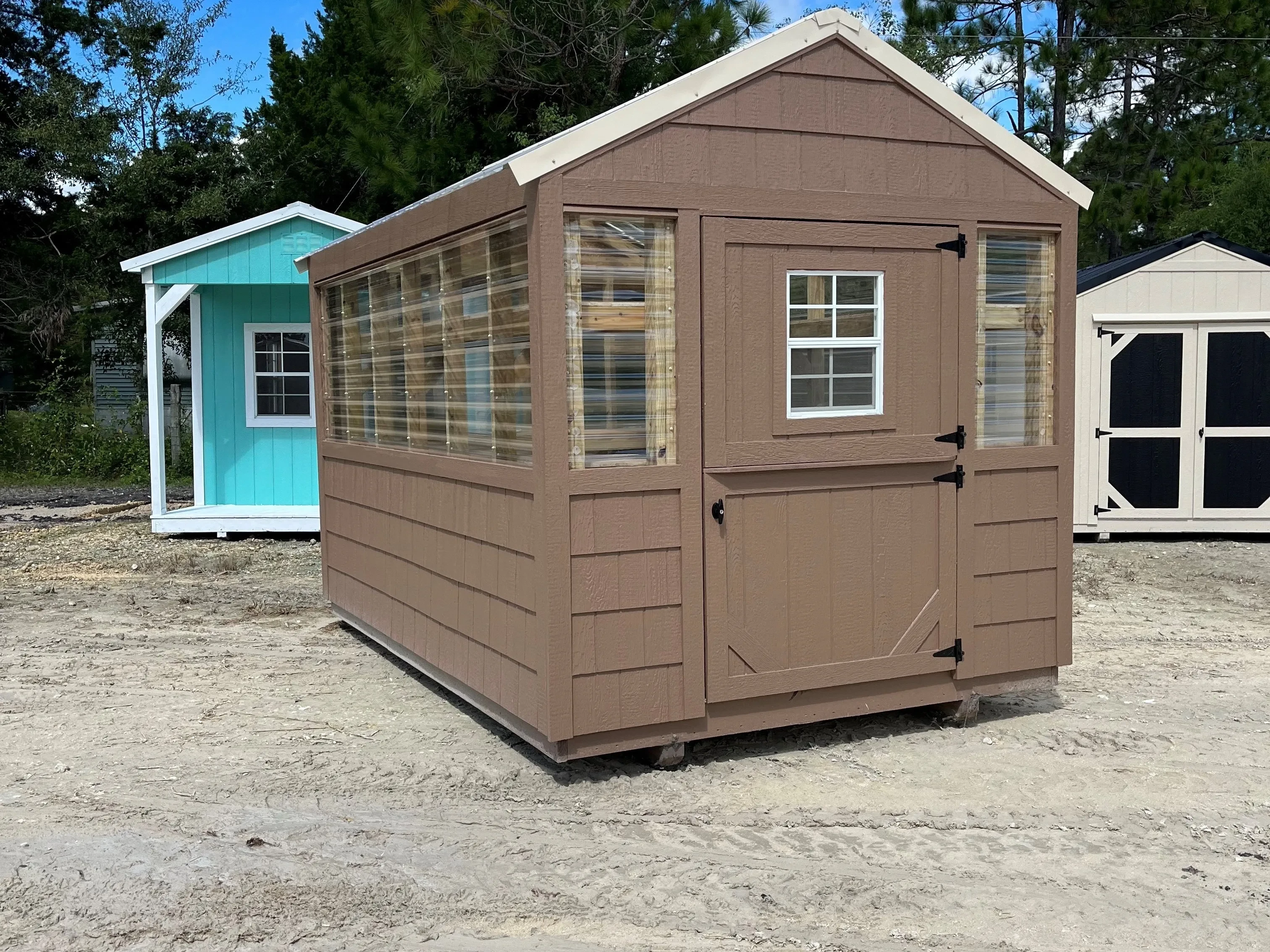 Outside of an 8x12 brown painted greenhouse, showing entry door, and side of the building