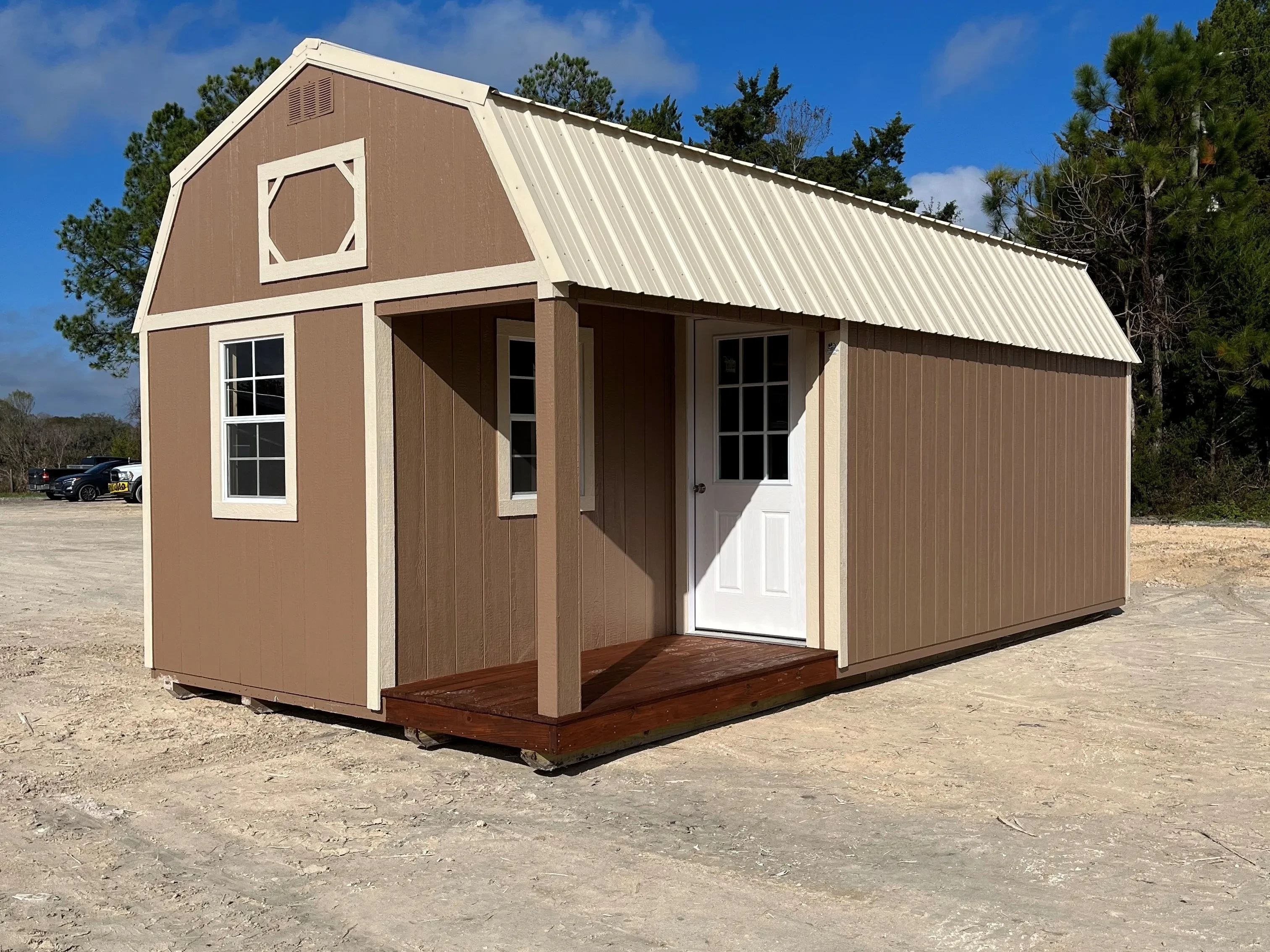Outside of a brown 12x24 lofted corner porch cabin showing entry door, porch, and two windows