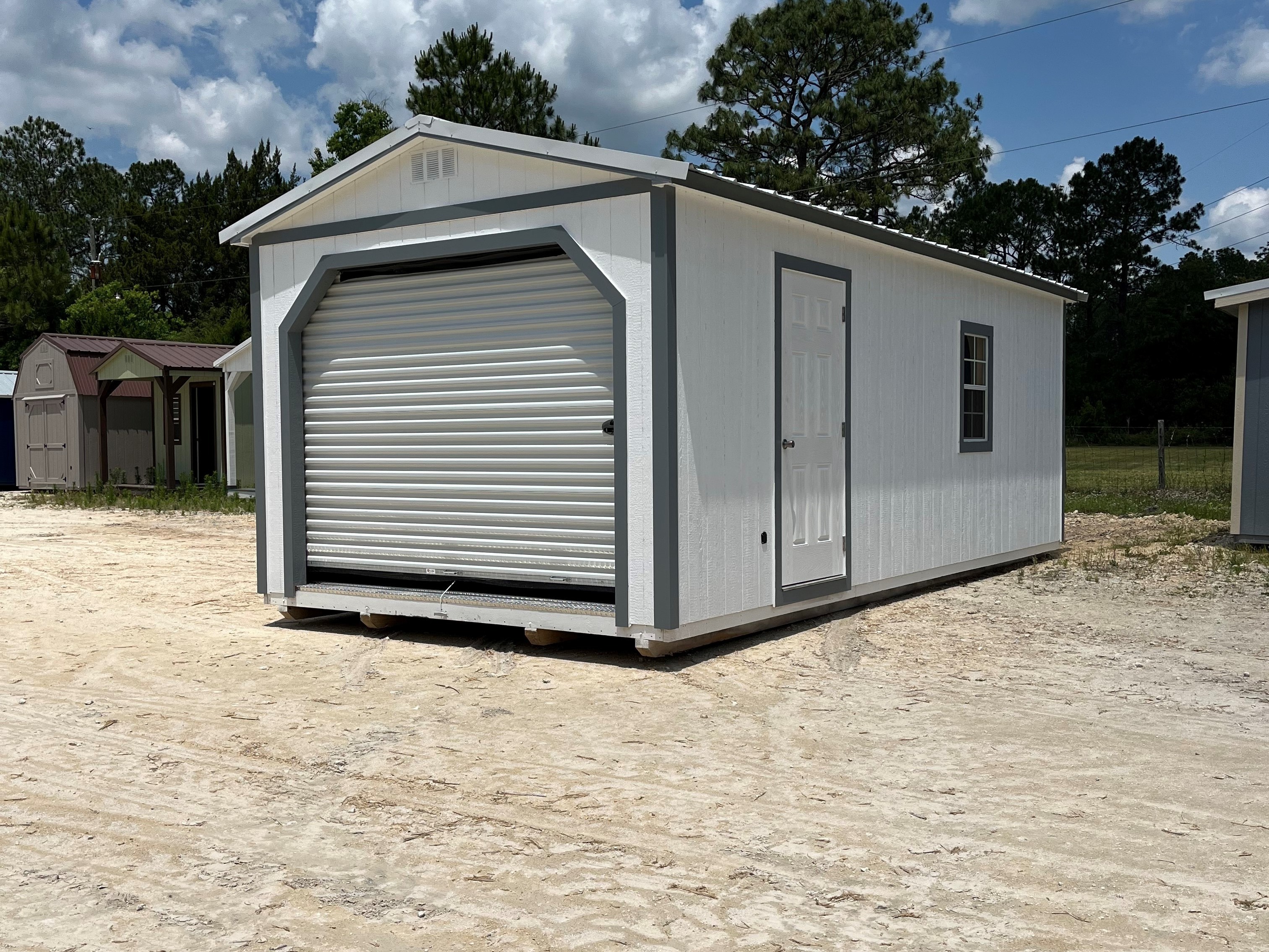 Outside of white 12x24 workshop showing a rollup door in front, entry door and window on side of building