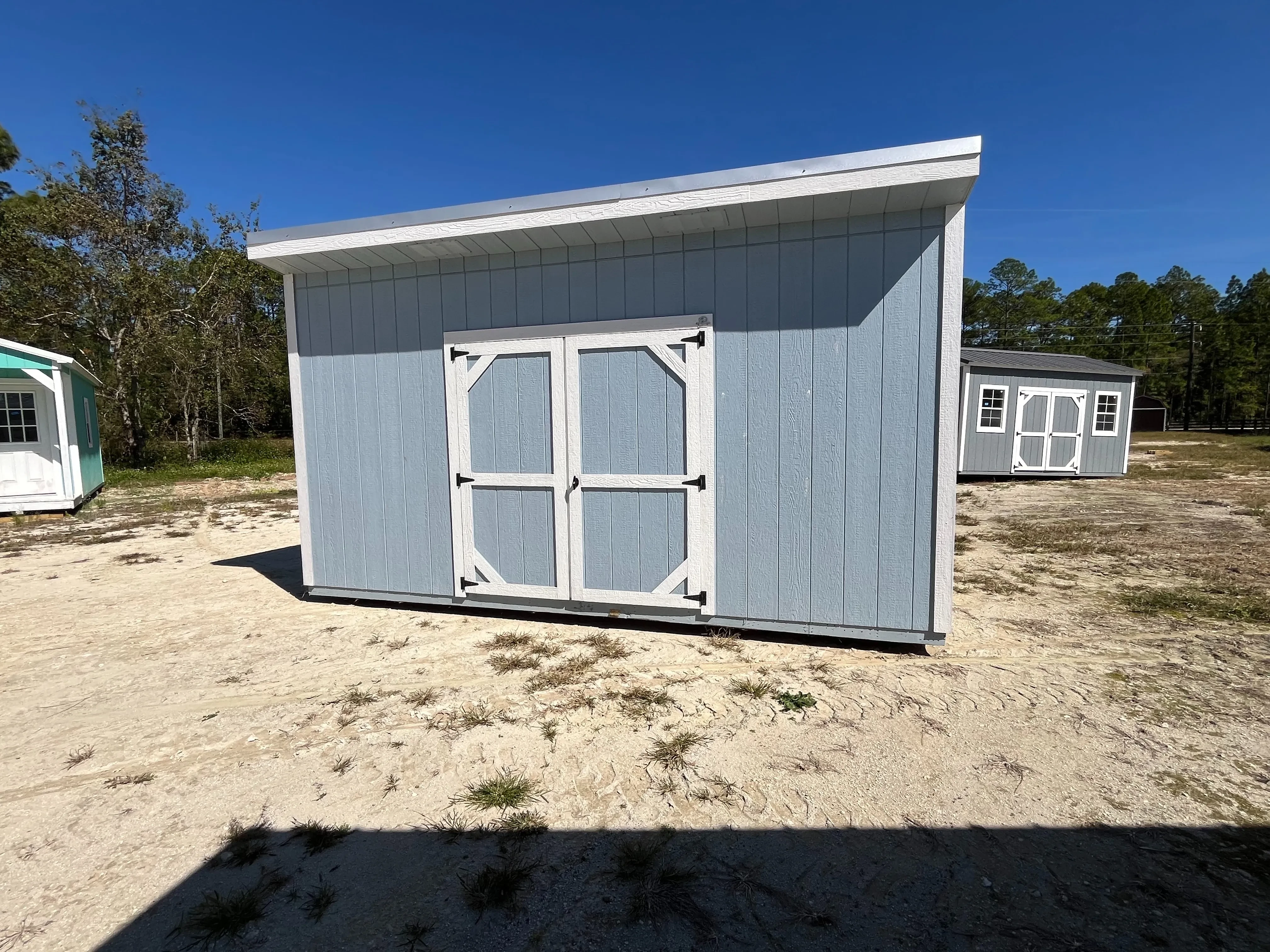 Exterior of a blue with white trim 10x16 urban shed that has a double wood door