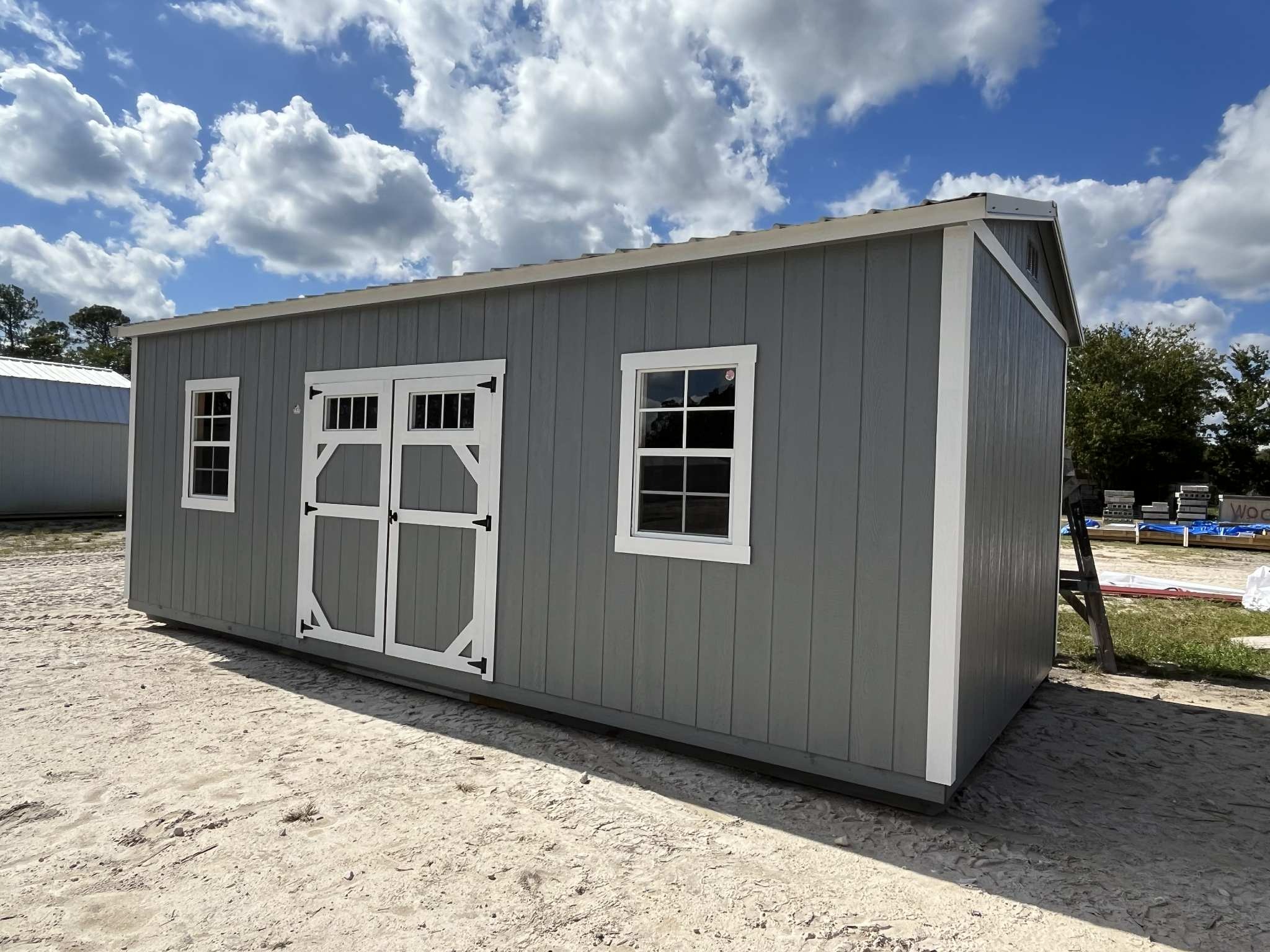 Exterior right of a light grey 10x20 side garden shed with double wood doors with transom window and windows