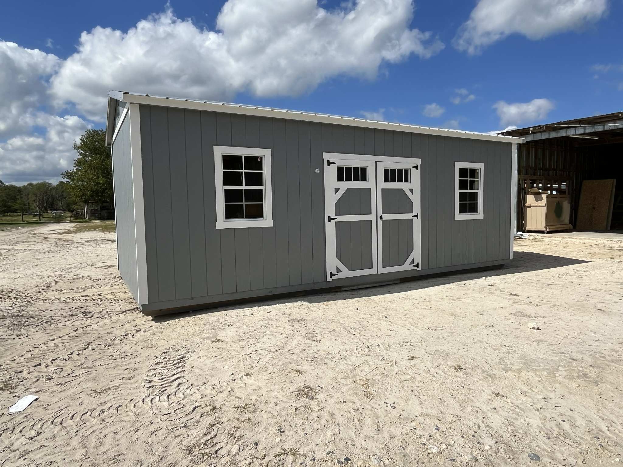 Exterior left of a light grey 10x20 side garden shed with double wood doors with transom window and windows