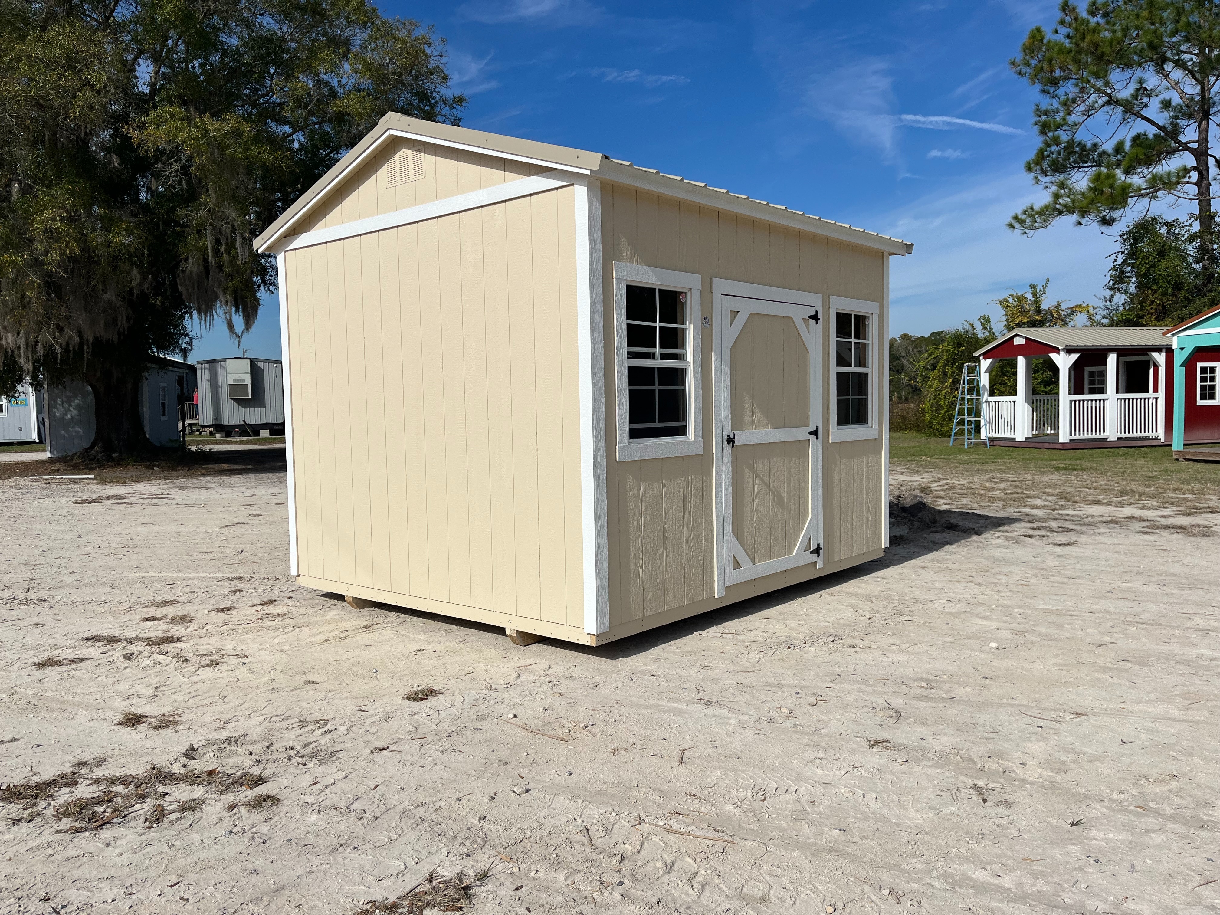 Exterior left view of an almond and white 10x12 side garden shed with a single wood door and windows