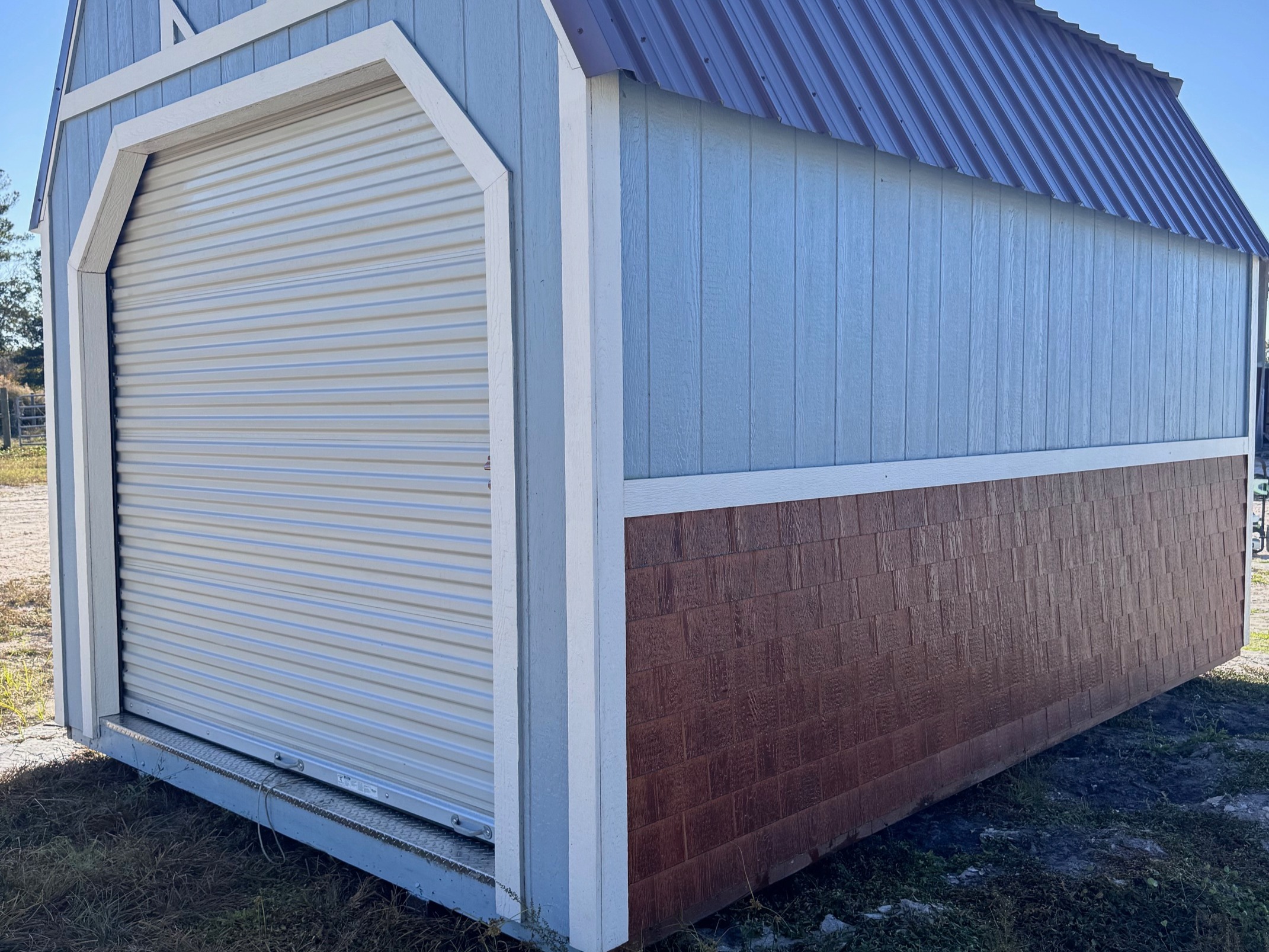 Back view of 10x16 Lofted Barn Cabin showing roll-up door and brown shake siding