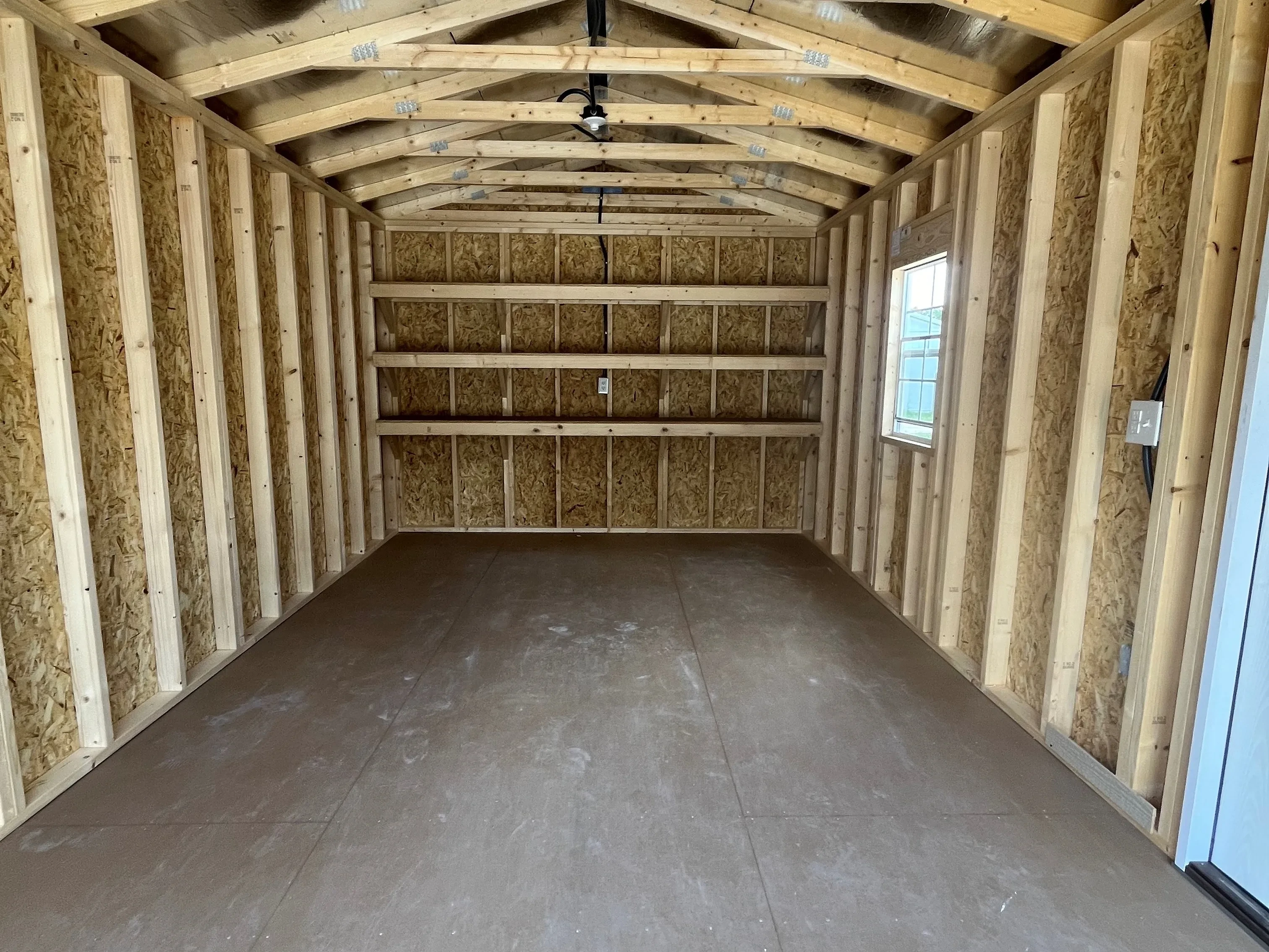 Interior view of a 12x20 workshop showing through the roll up door a walk-in door, window and shelving
