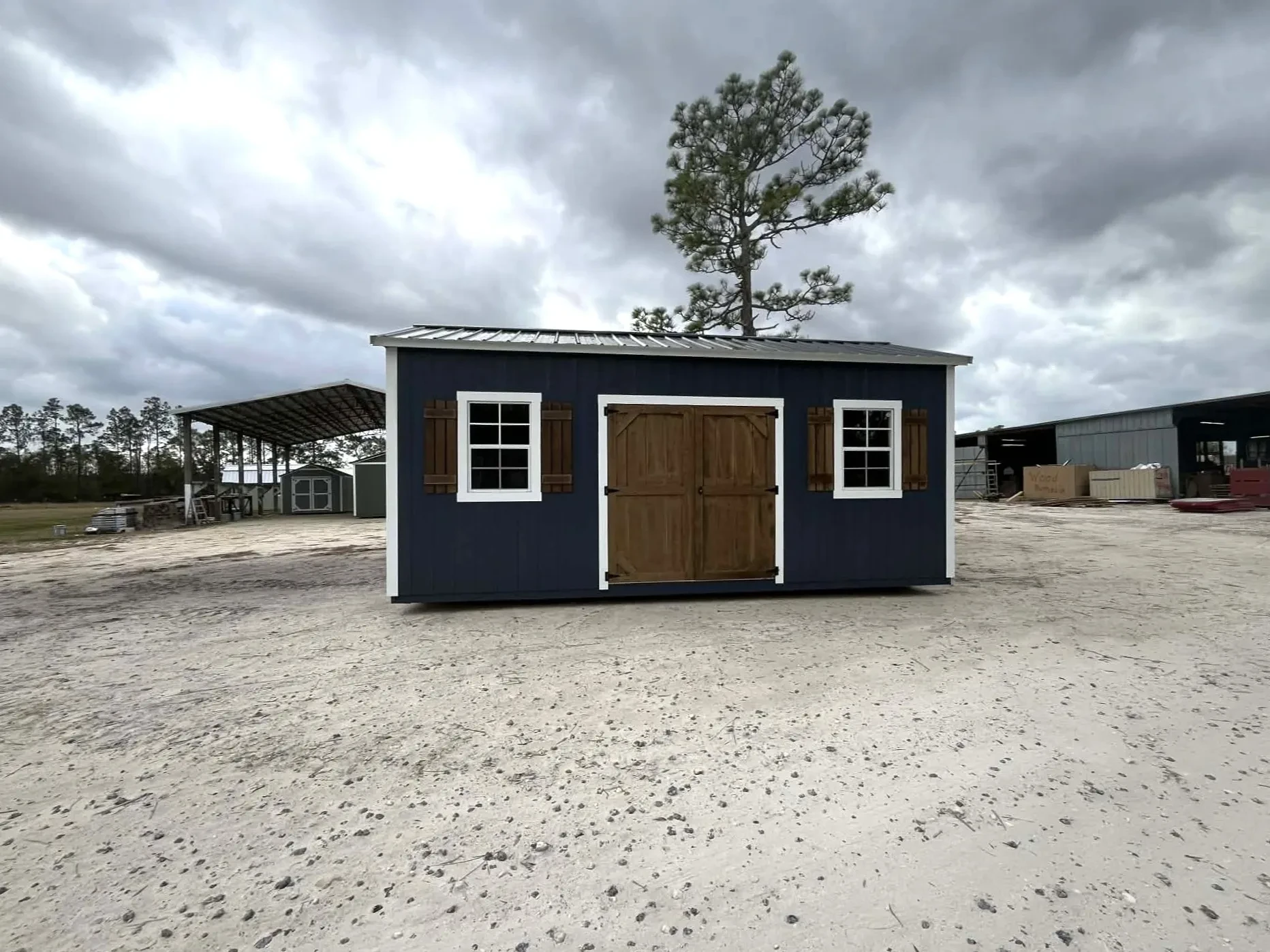 Exterior of a dark blue 10x20 side garden shed showing double wood doors, windows and shutters