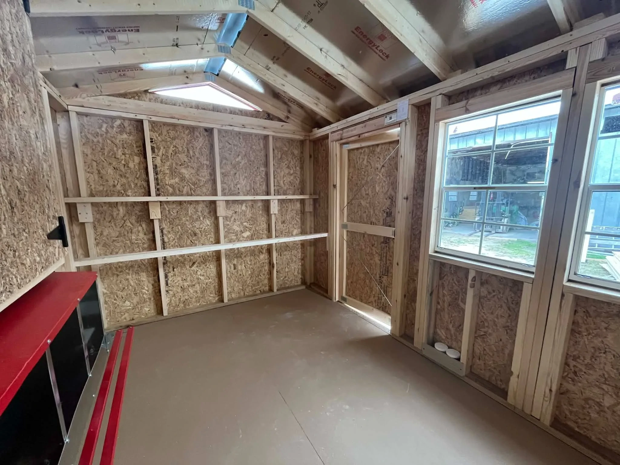 Interior of an 8x12chicken coop viewing from the back wall showing the door, windows and roosting bars
