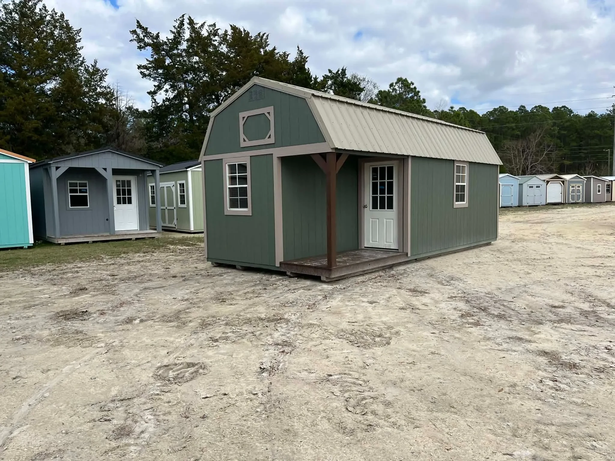 Exterior front of a green 12x24 lofted corner porch cabin showing the porch area with a walk-in door and windows
