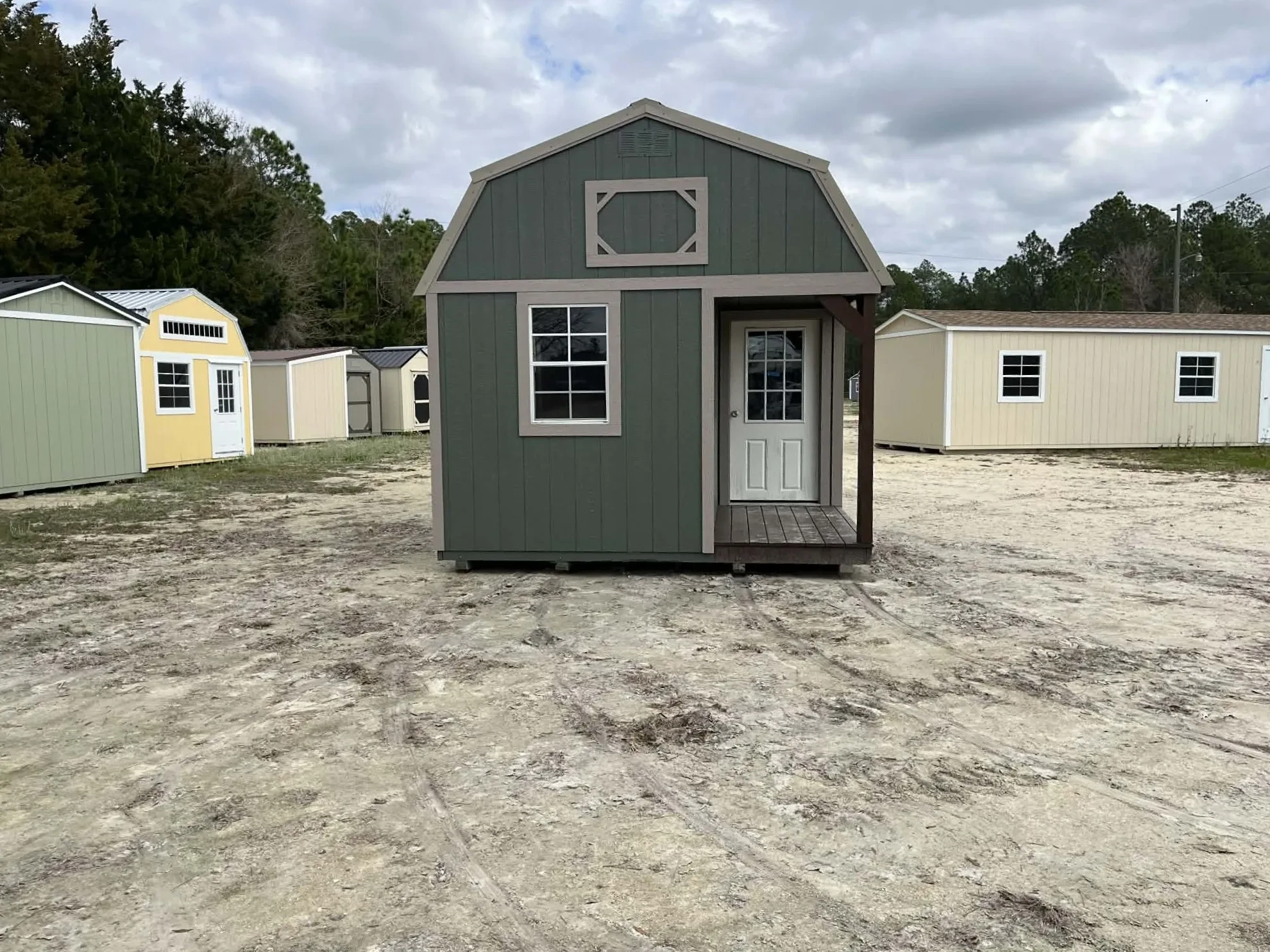 Exterior front of a green 12x24 lofted corner porch cabin showing the porch area with a walk-in door and window