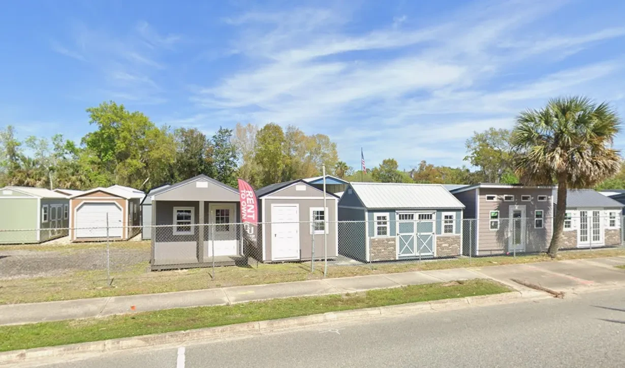 a shed lot in florida seen from the road with a palm tree and colorful banner flags