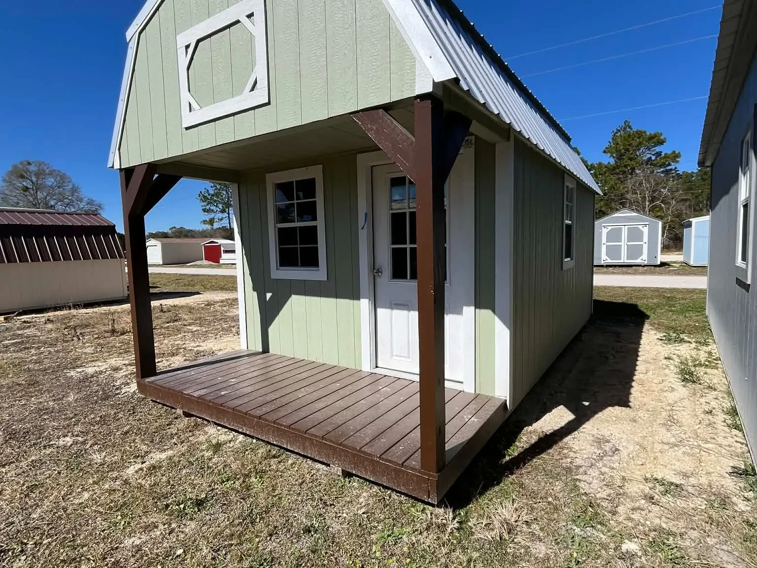 Exterior of a green 10x20 Lofted Barn Cabin showing a porch, walk-in Door and windows