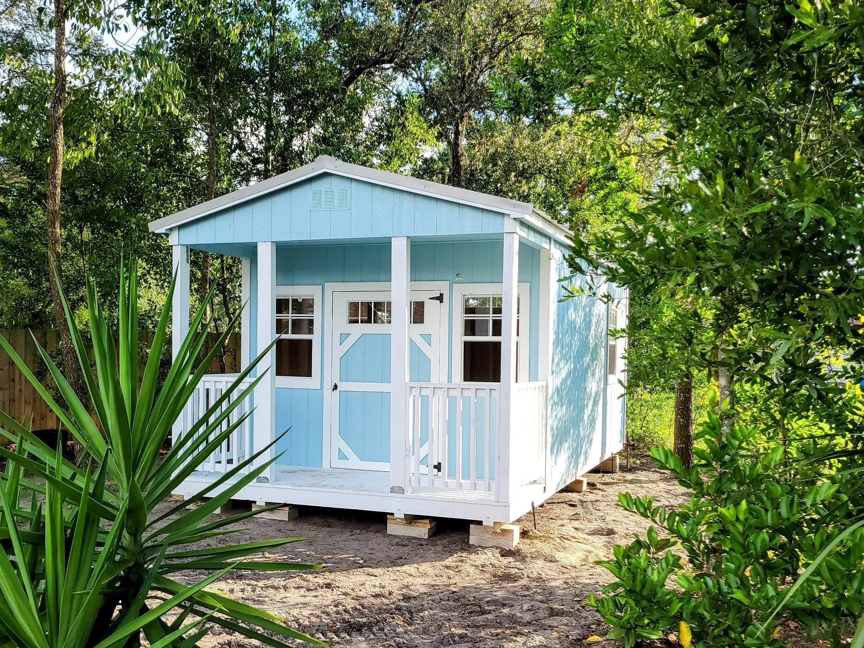 cute light blue cabin with white trim and a white porch sitting among green Florida foliage