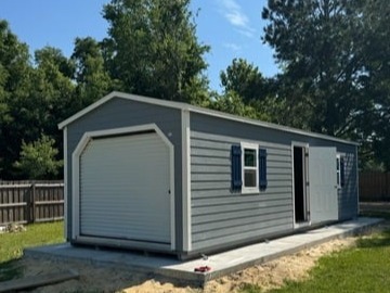 gray workshop shed with a garage door in the end and windows and a walk-in door in the side