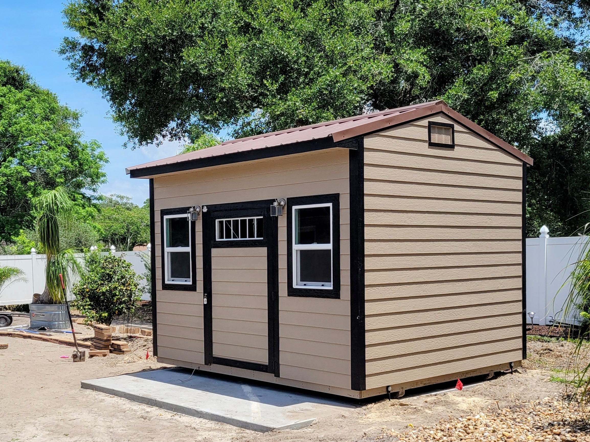 brown garden shed with door and windows in the side sitting in a backyard