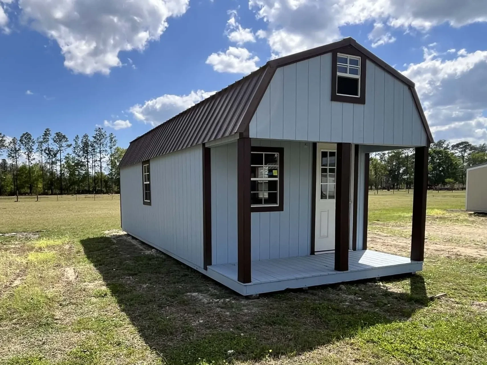 Exterior view of a light blue 12x28 lofted barn cabin showing the porch, walk-in door and windows