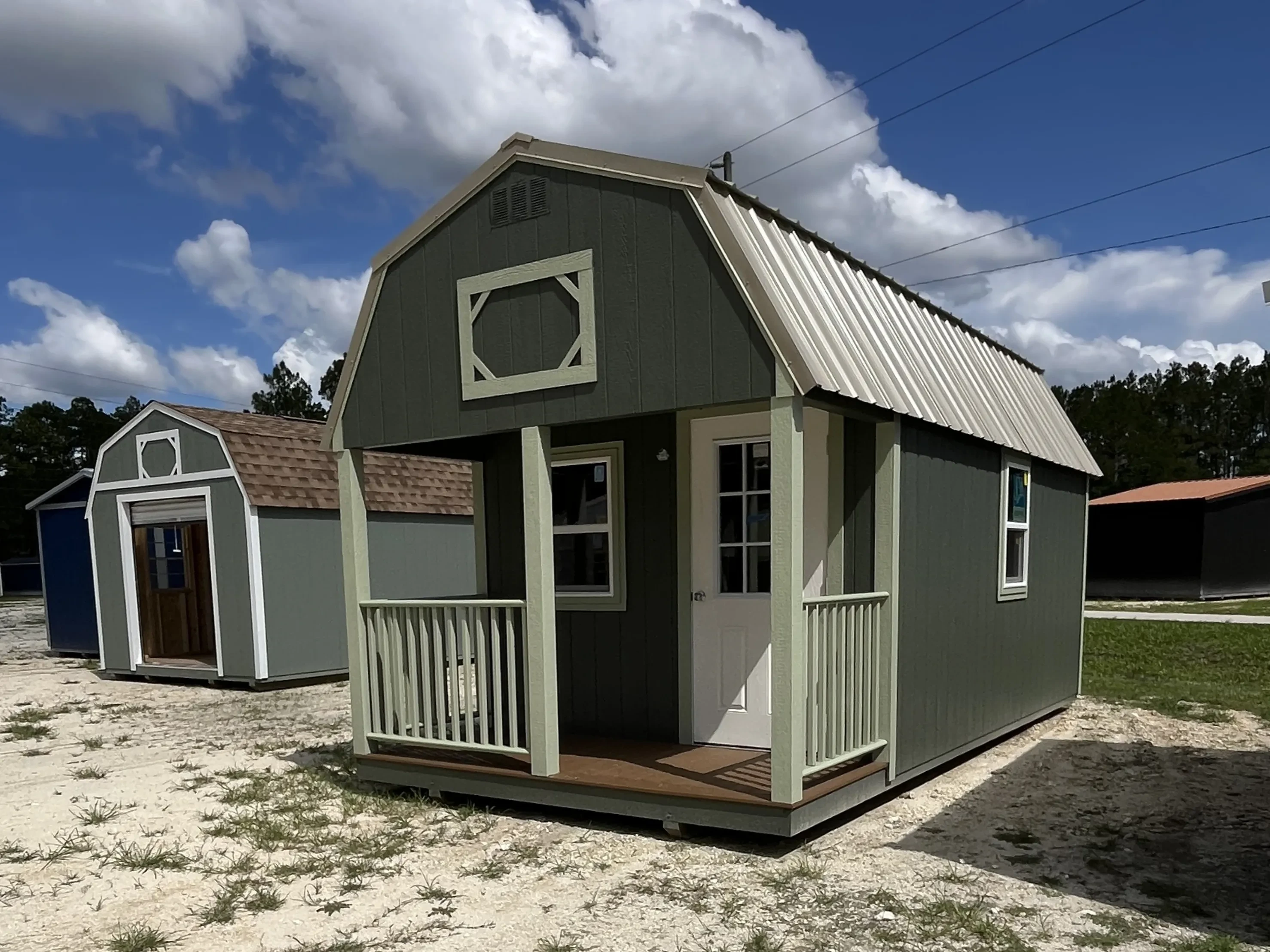 Outside of a dark green 10x20 lofted barn cabin showing an entry door, windows, and front porch with light green railing
