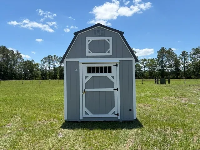 Exterior front view of a grey 8x12 lofted barn showing the door with transom window.