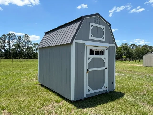 Exterior front left view of a grey 8x12 lofted barn showing the door with transom window.