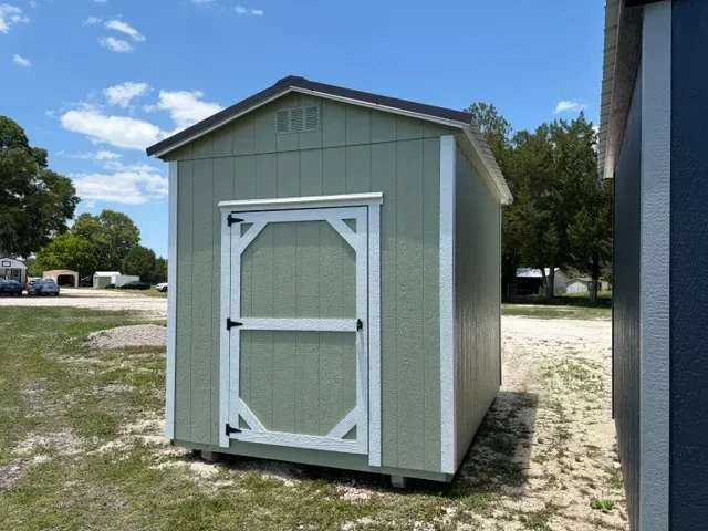 Exterior front view of a sage green 8x12 garden shed showing the wood door
