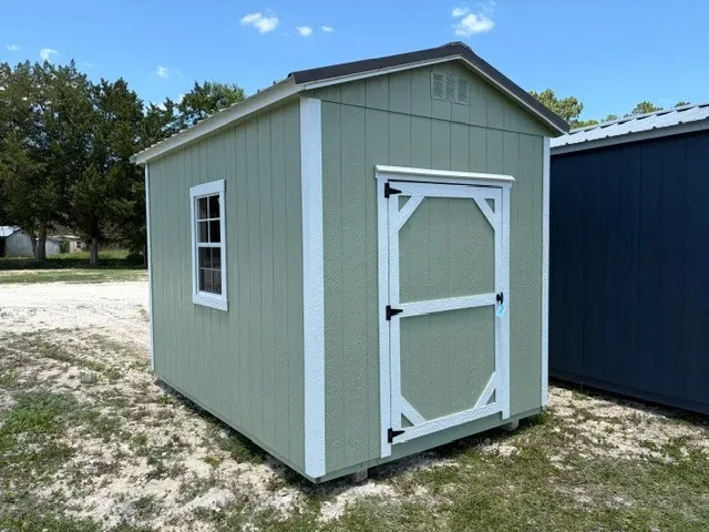 Exterior front view and left side of a sage green 8x12 garden shed showing the wood door and window