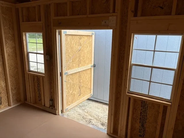 Interior of an 8x12 side garden shed showing the inside of the single wood door and two windows.